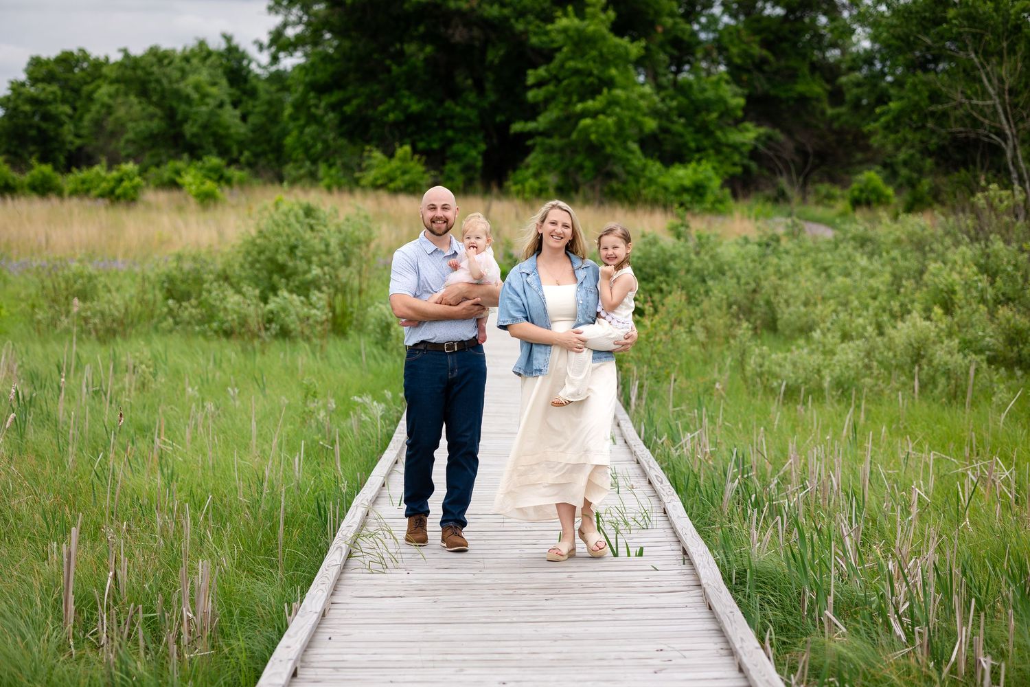 Family of four posing on a wooden boardwalk surrounded by lush green meadows during an outdoor portrait session.