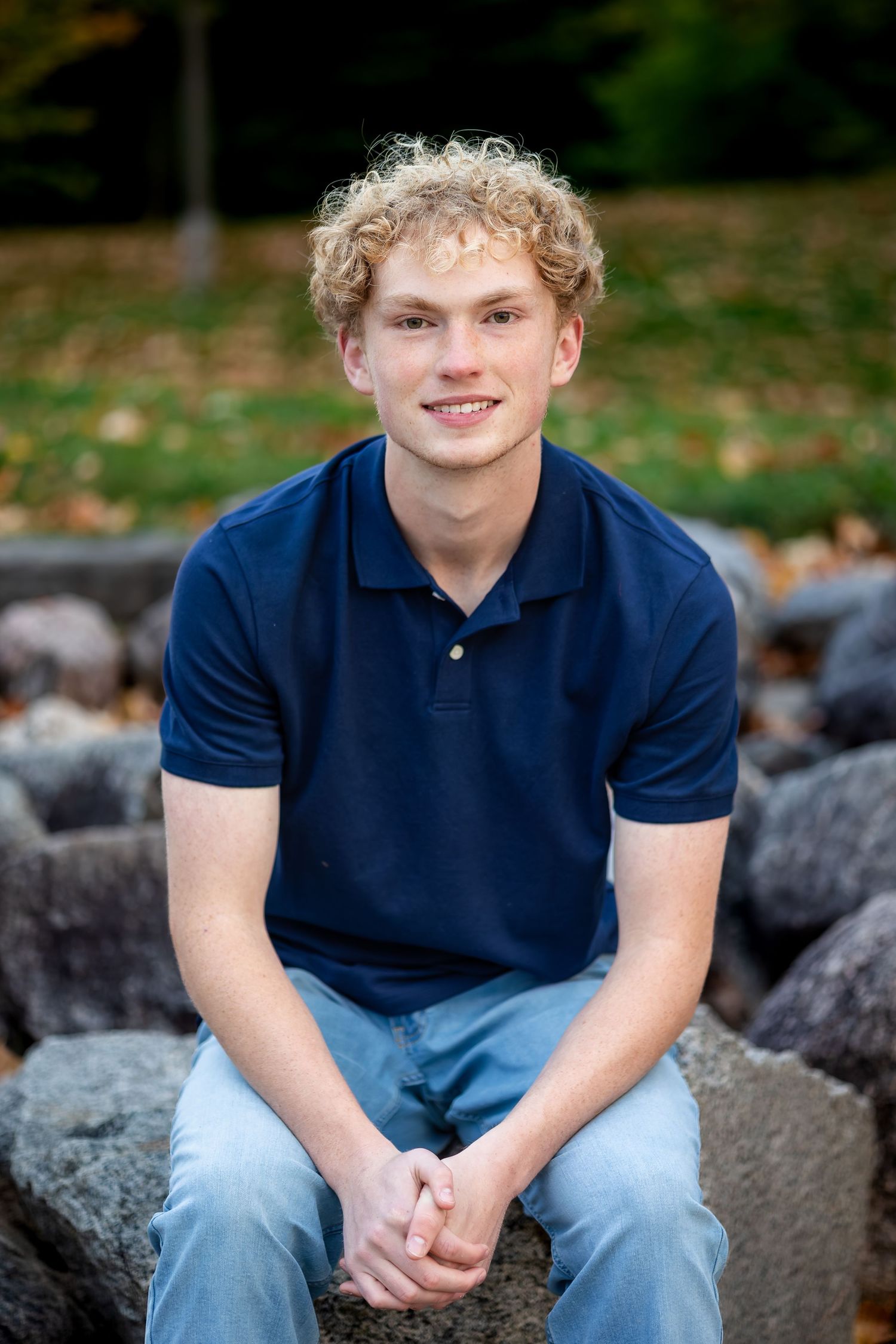 A series of four casual outdoor portrait photos showing someone sitting on rocks wearing a navy polo shirt and jeans.