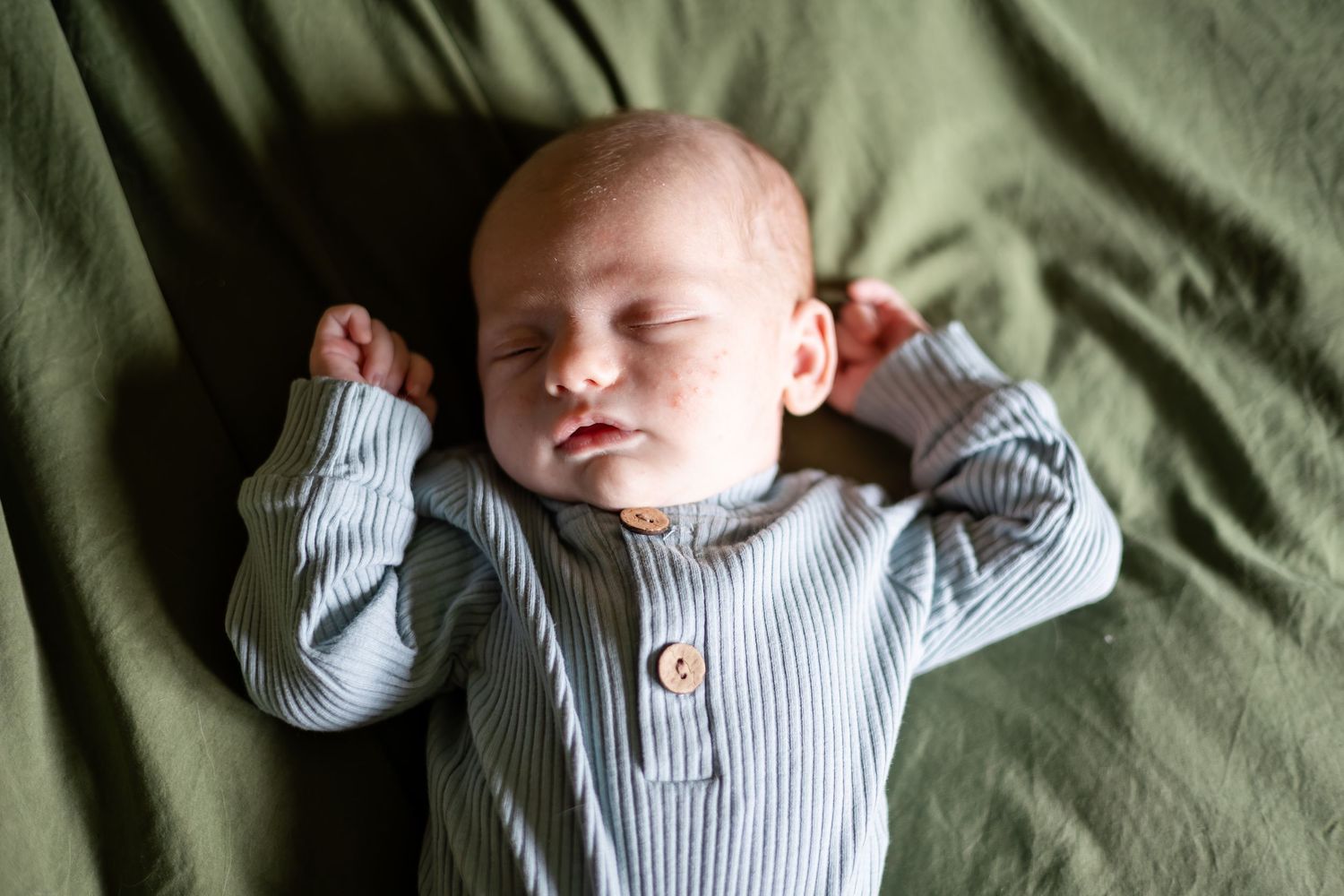 Sleeping infant wearing blue striped outfit on olive green bedding.
