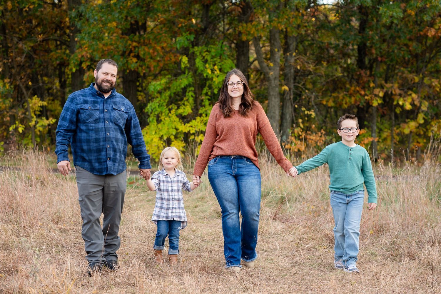 Family walking together in a line through autumn field with trees in background.