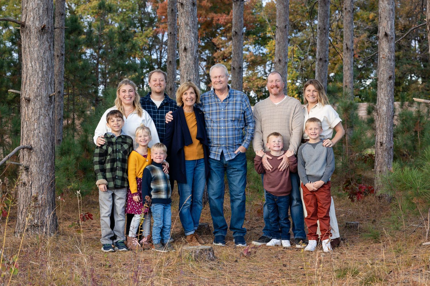 Large family group photo taken outdoors among tall pine trees in autumn.