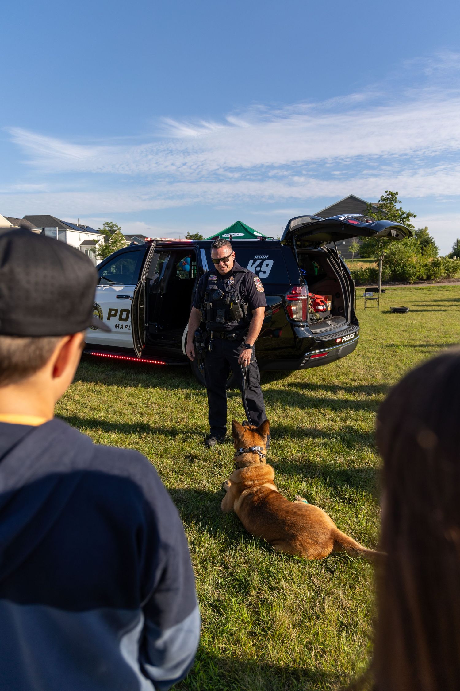 K-9 police officer with service dog gives demonstration to gathered crowd by patrol vehicle.