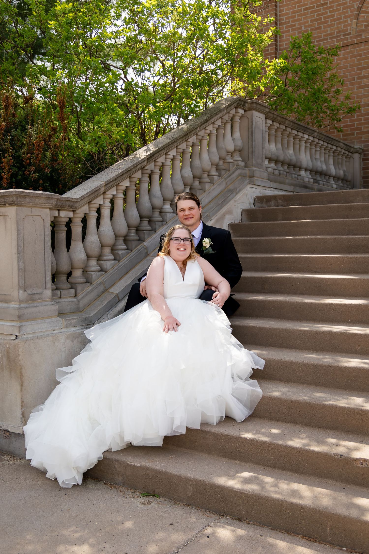 Smiling bride and groom pose together on elegant stone staircase with balustrade on their wedding day.