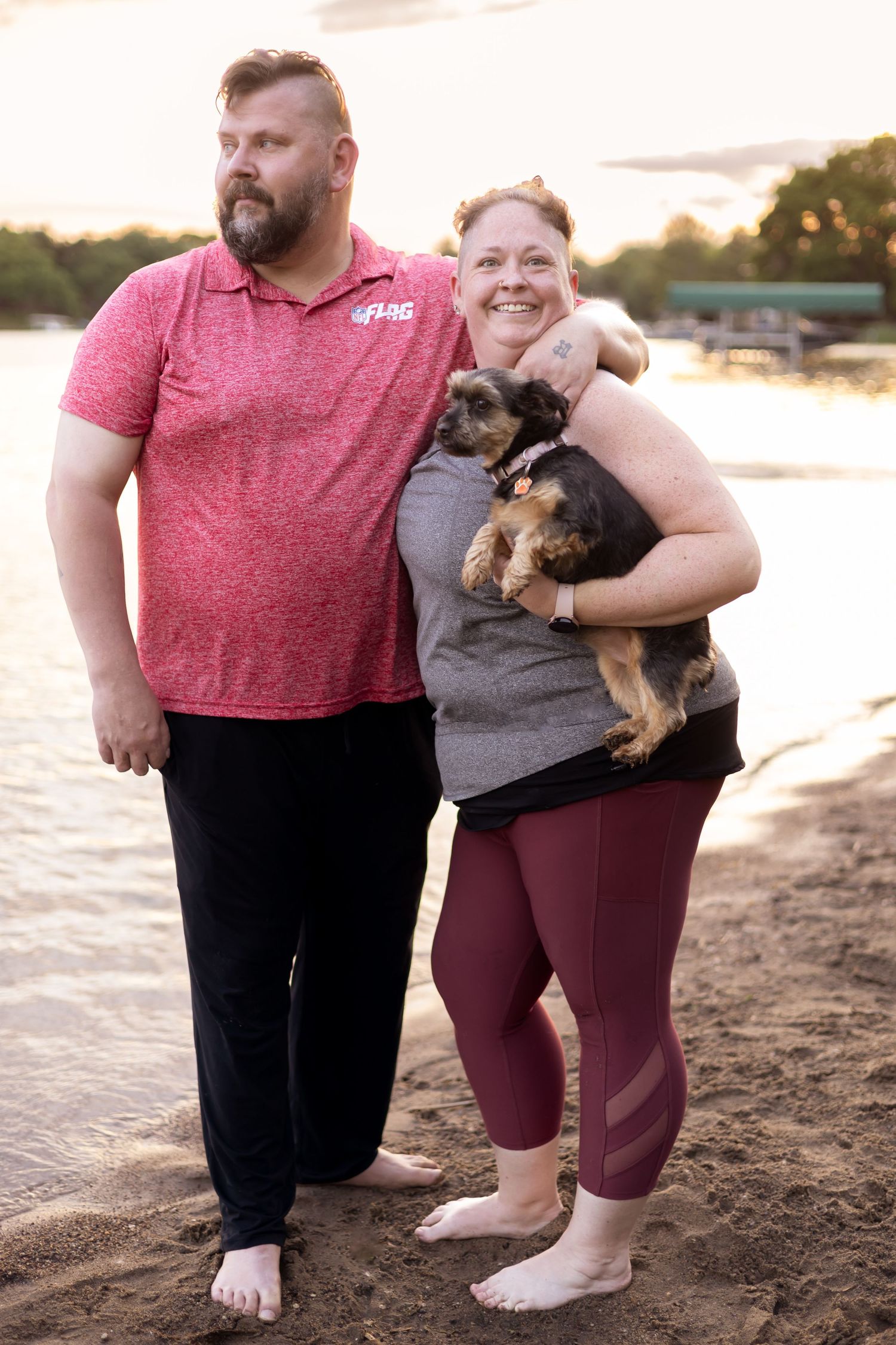 A couple stands on a beach at sunset holding their small dog.