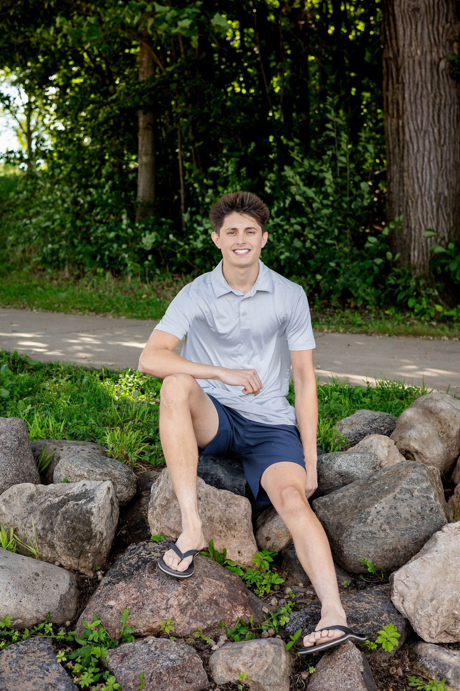 Person in casual attire relaxing on large rocks surrounded by lush greenery on a sunny day.