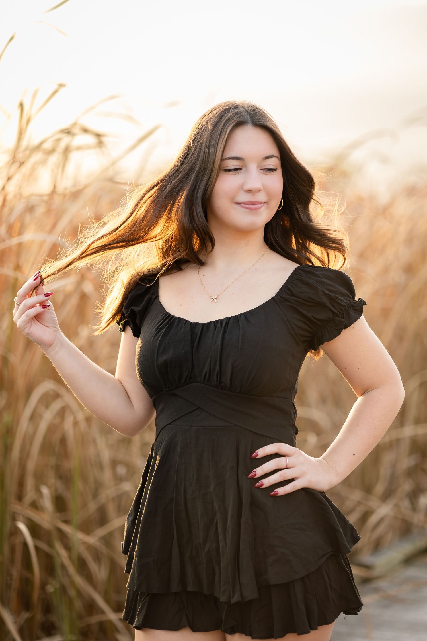 Dancing in black dress among tall grass at golden hour.