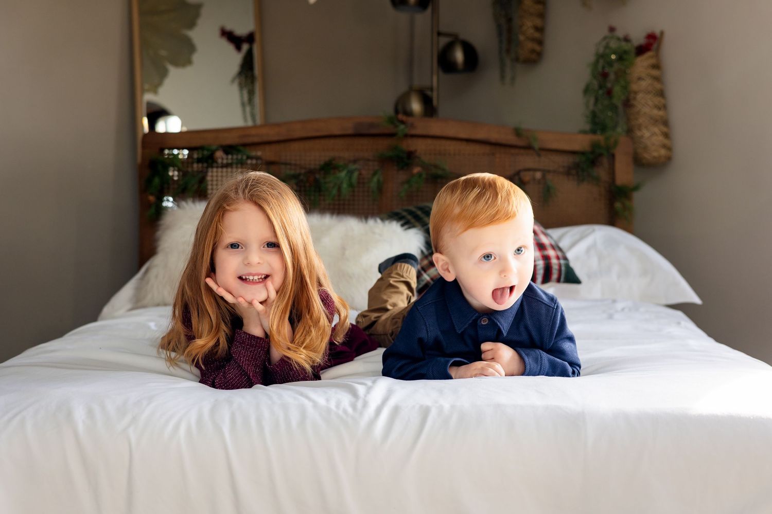 Two young children lying on a white bed, smiling and laughing, with festive holiday decorations in the background.