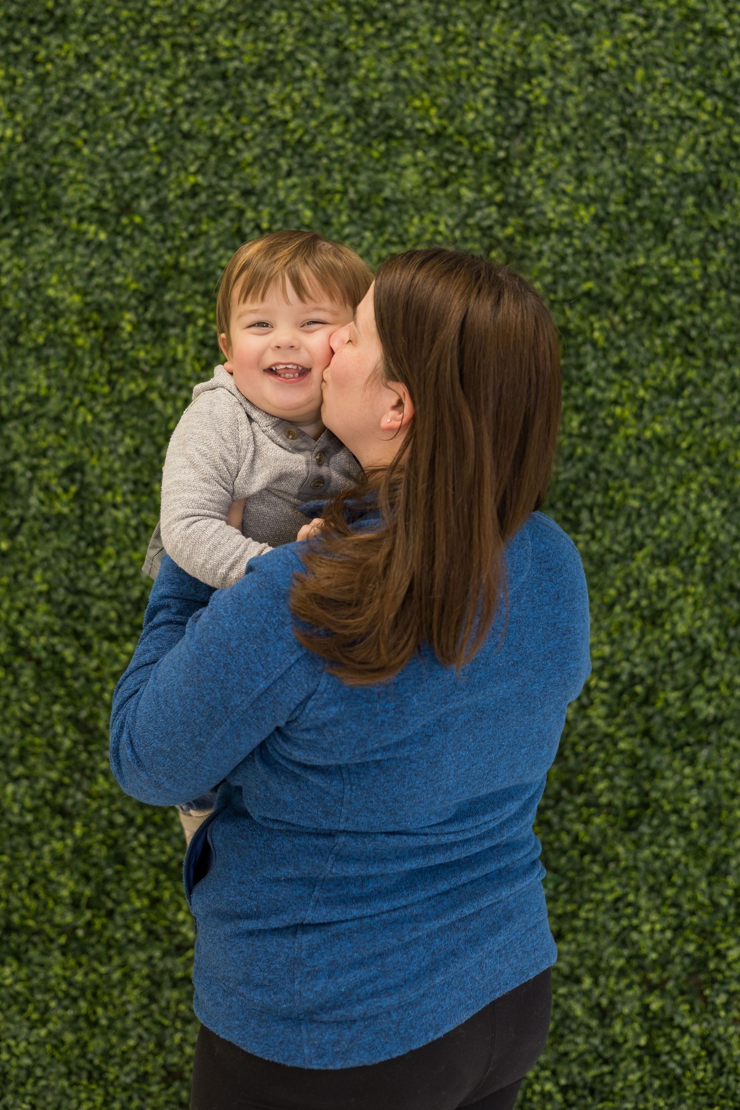 A joyful moment shared between parent and child against a green hedge background.