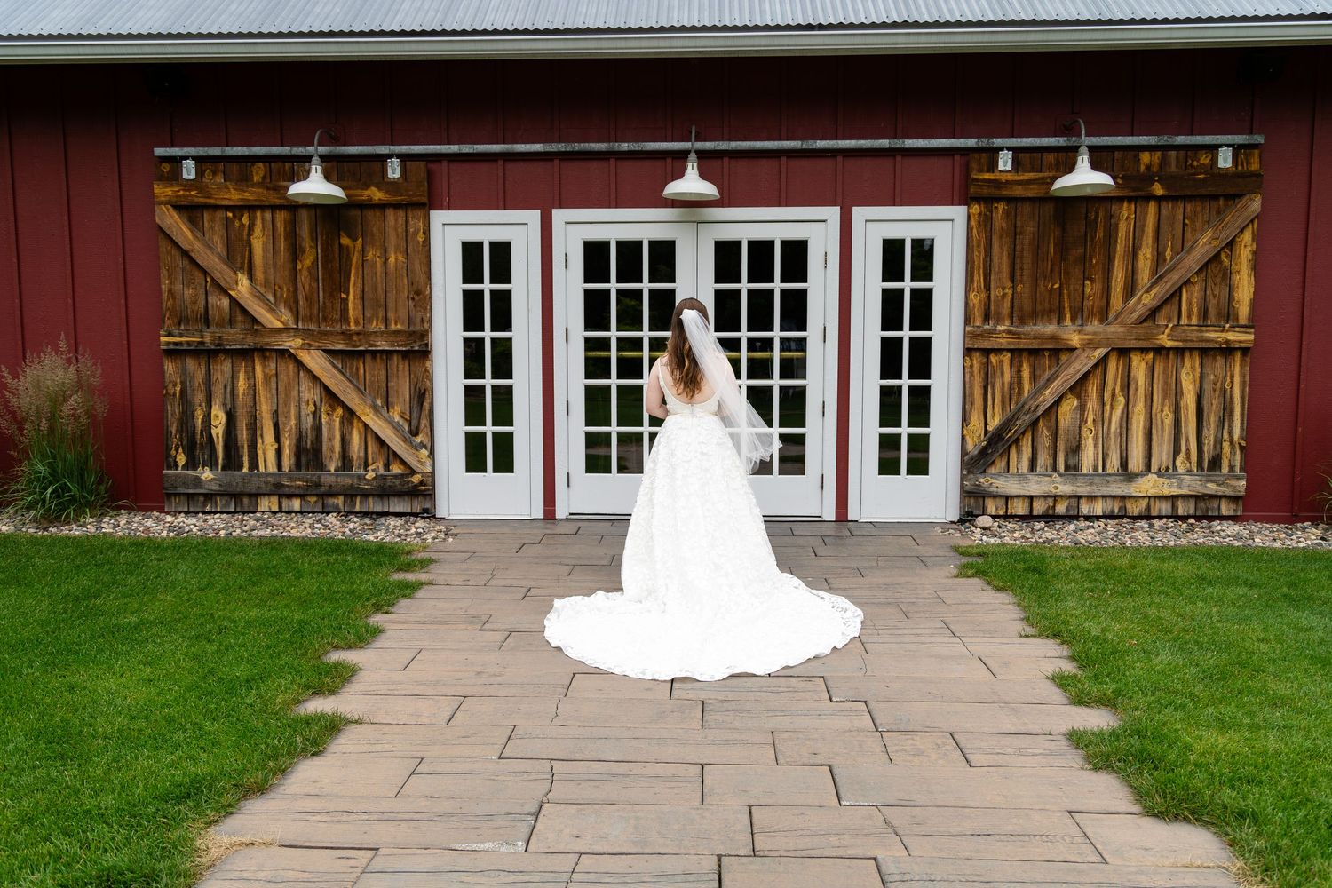 A bride in a white wedding dress poses in front of a rustic red barn venue.