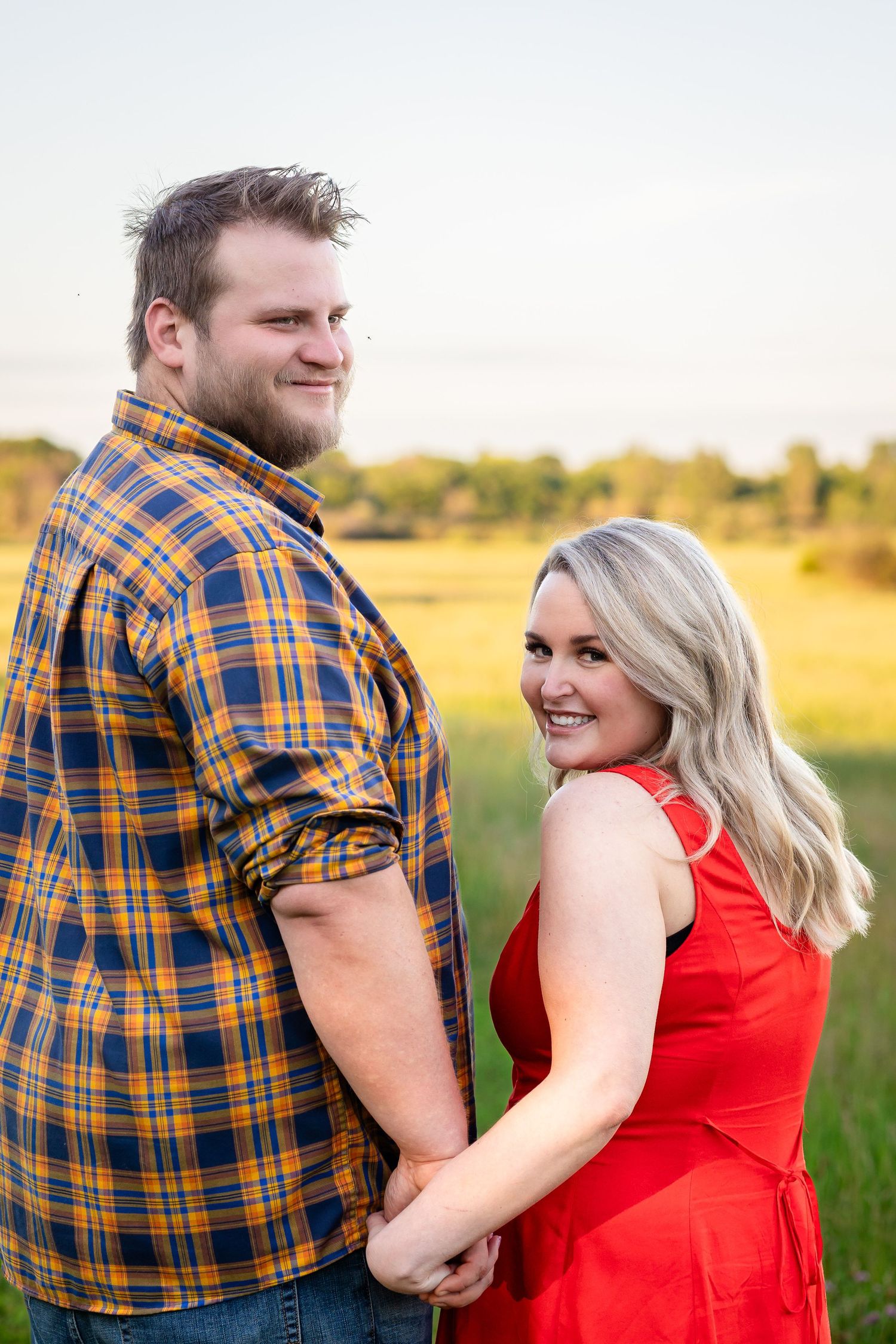 A couple laughs together in a sunny field during a photo session.