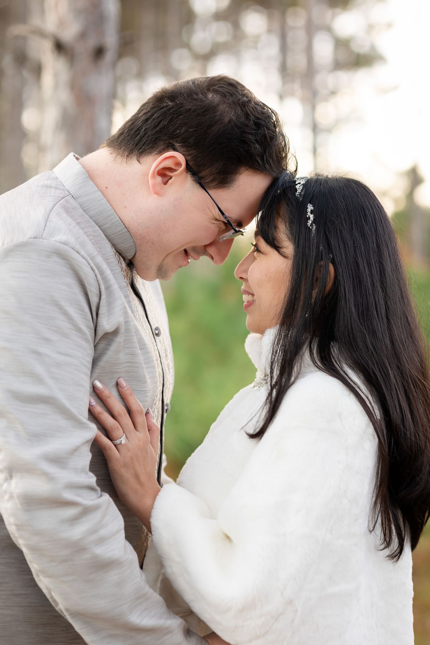 An intimate moment between a couple in wedding attire sharing a close embrace among pine trees.