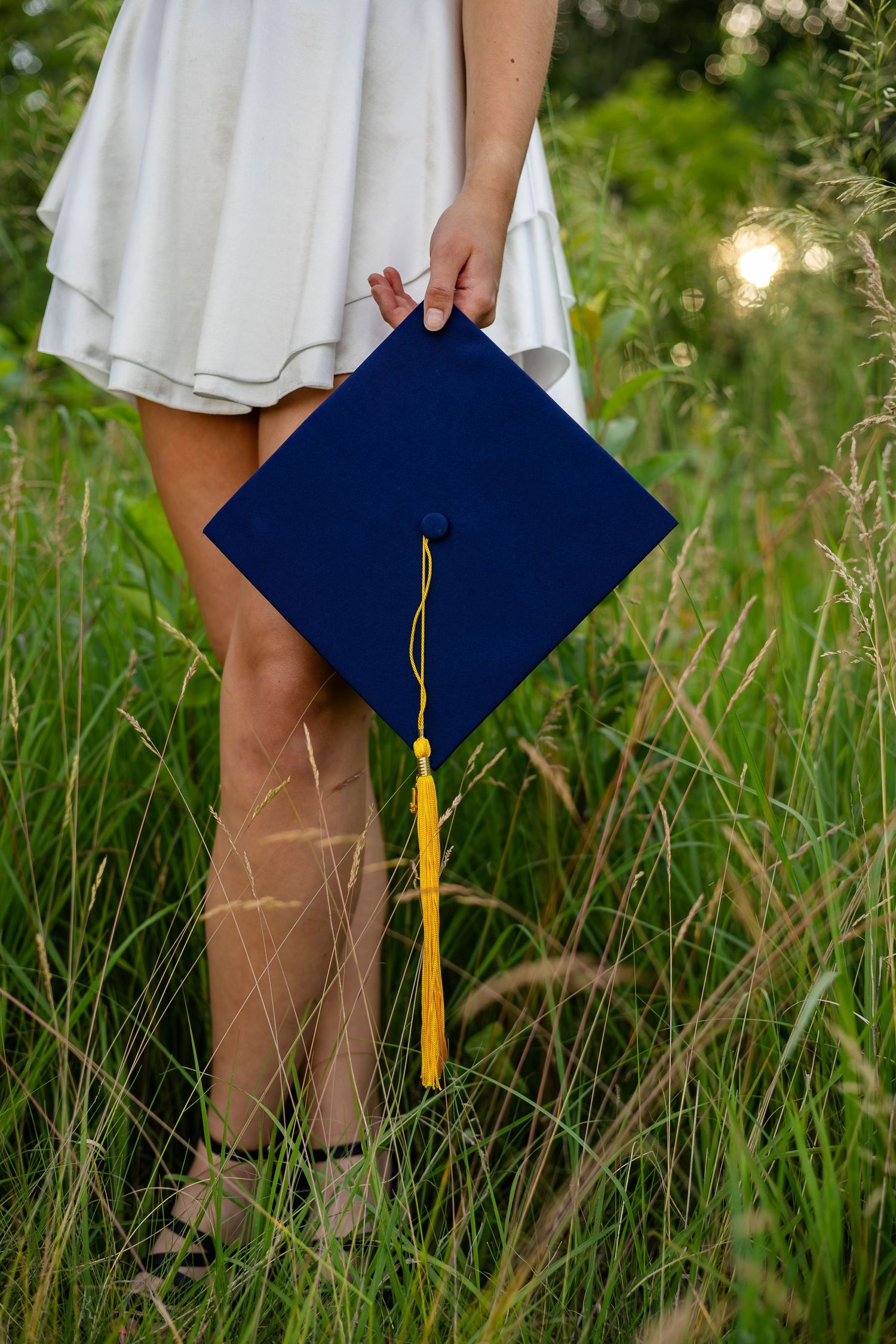 Navy blue graduation cap with gold tassel held in grassy field.