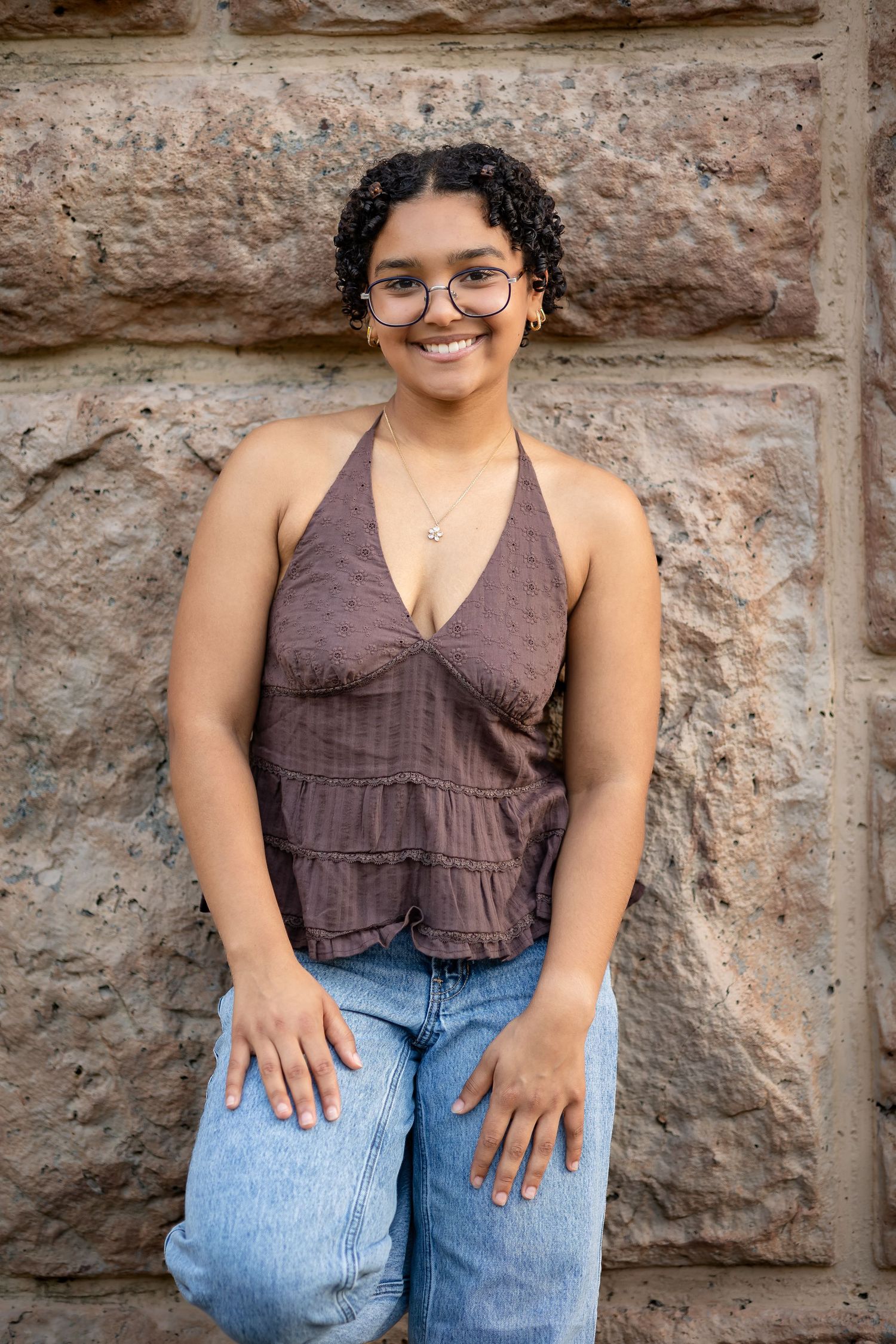 A series of casual portraits against a textured stone wall shows someone in a brown top and blue jeans.