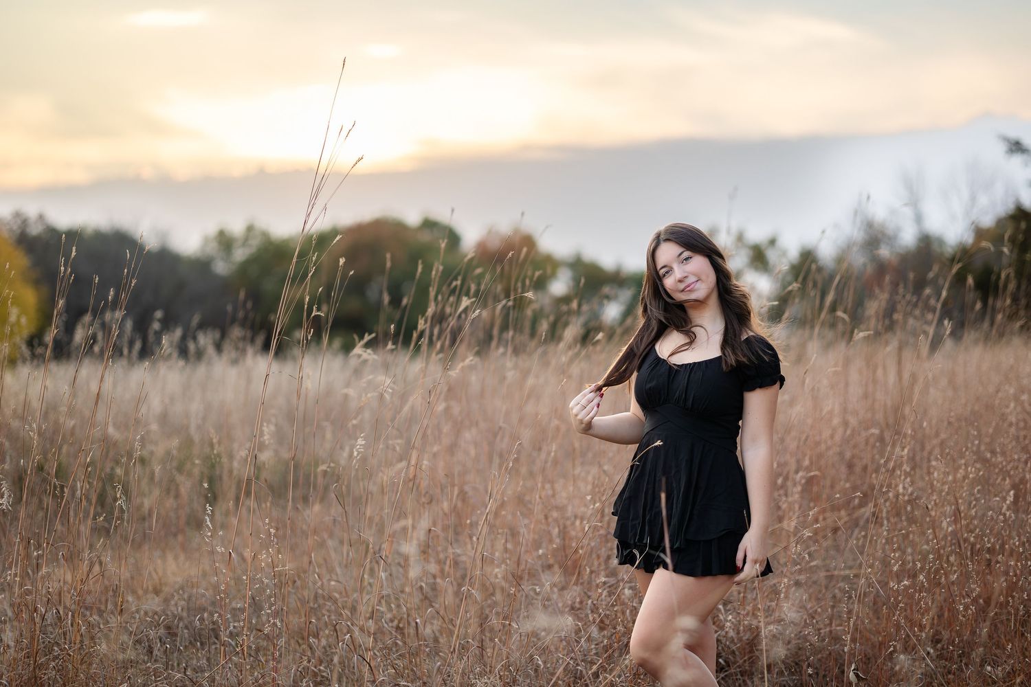 Person in black dress poses in golden field at sunset.