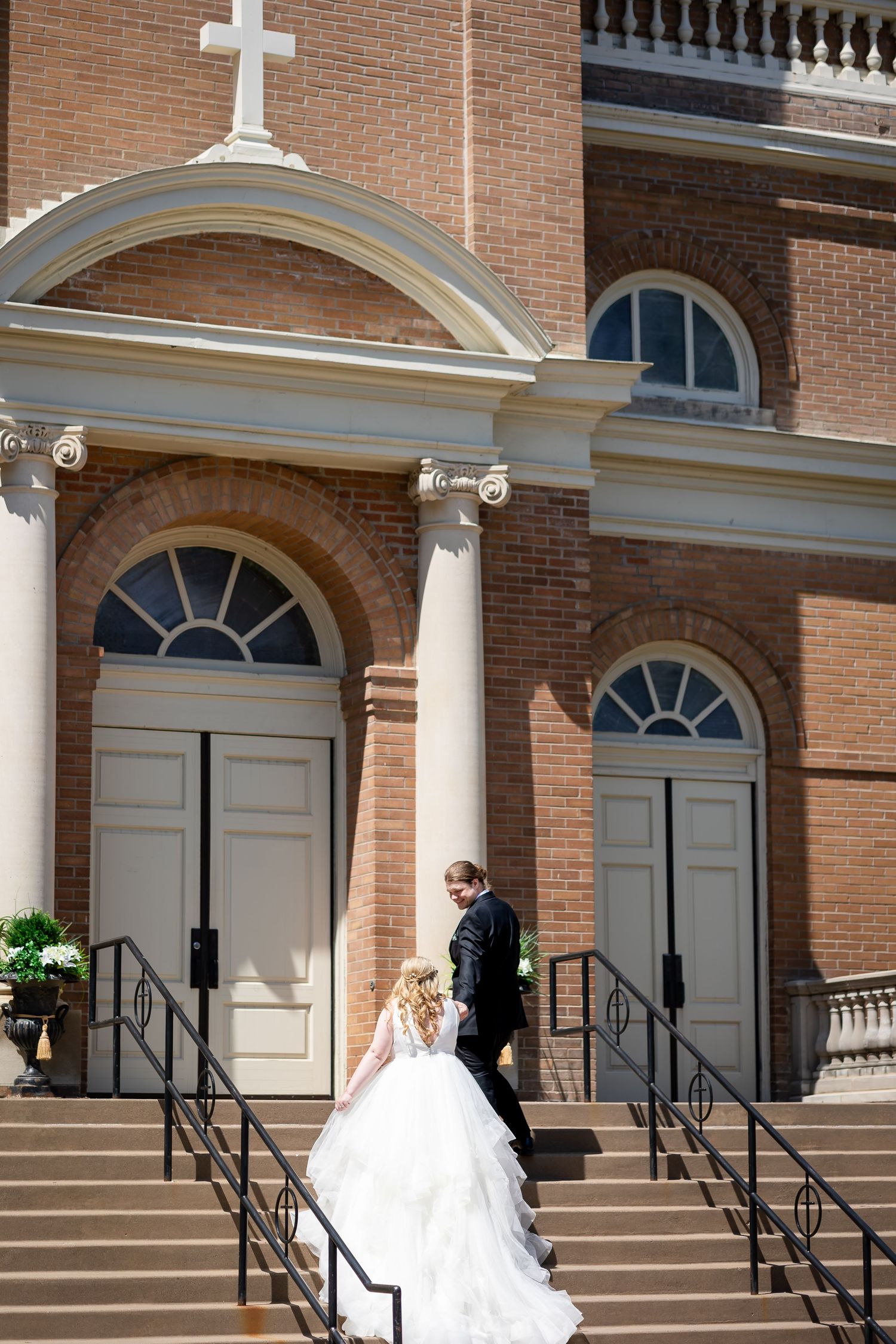 Bride and groom walking up church steps in wedding attire outside a classic brick church with white columns and cross.