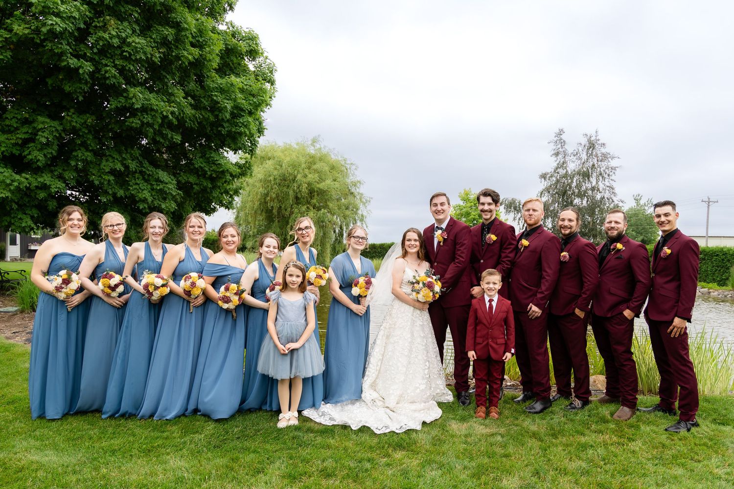 A full wedding party portrait series with burgundy and blue color scheme in an outdoor setting.