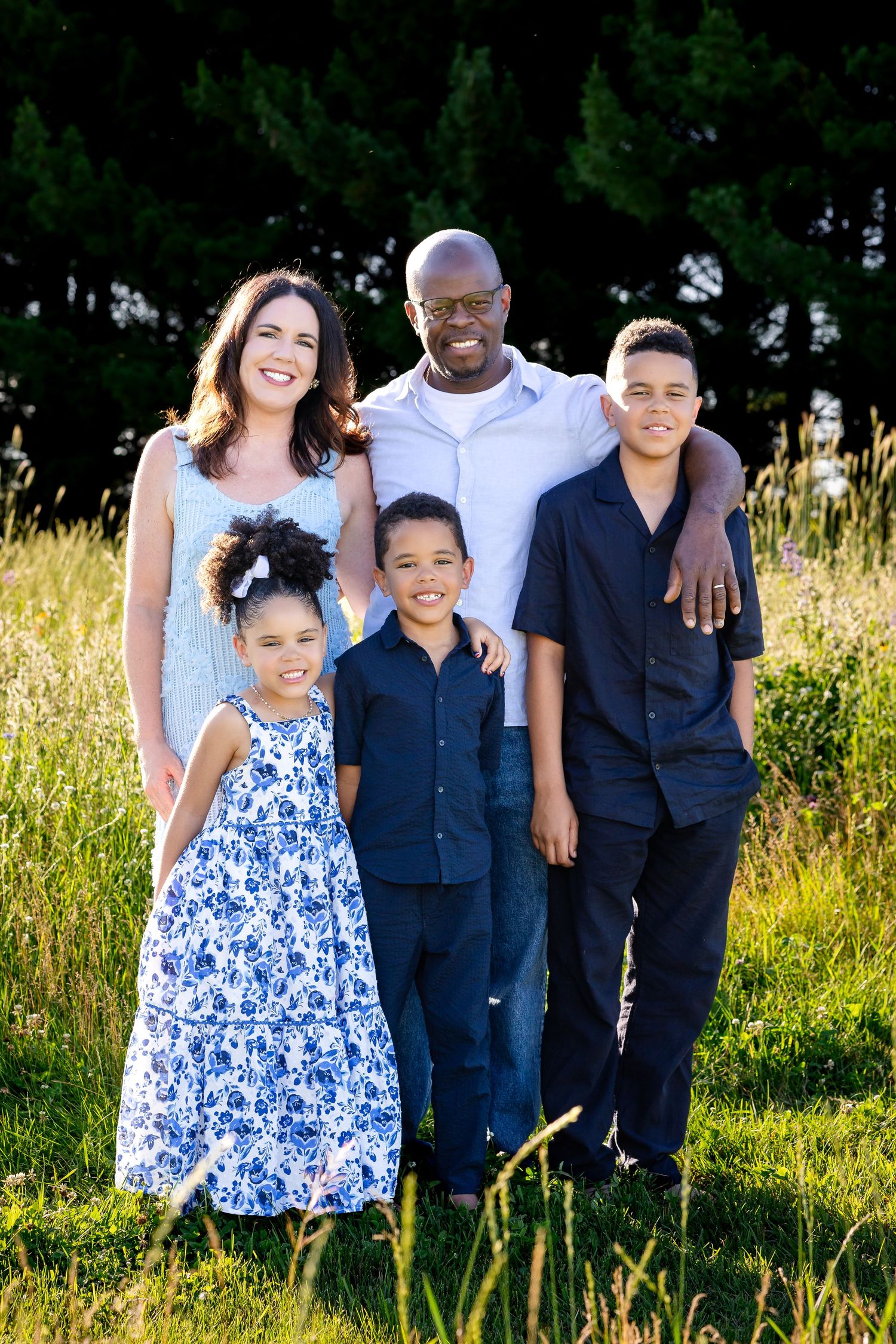 Family of five in coordinated navy and white outfits posing in sunny field.