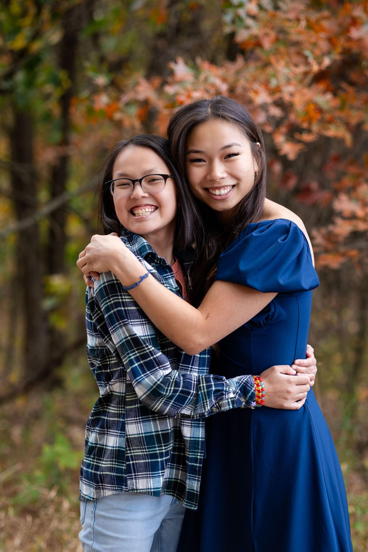 Three friends sharing joyful hugs and laughter against a backdrop of autumn foliage.