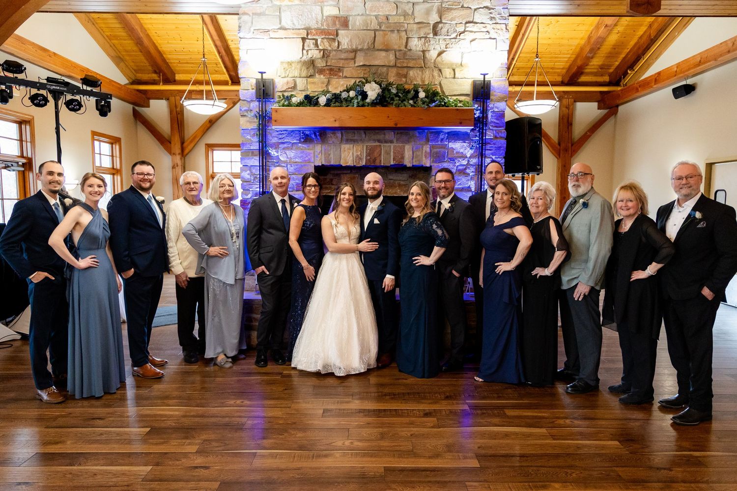 Bride and groom pose with family members in front of a stone fireplace at reception.