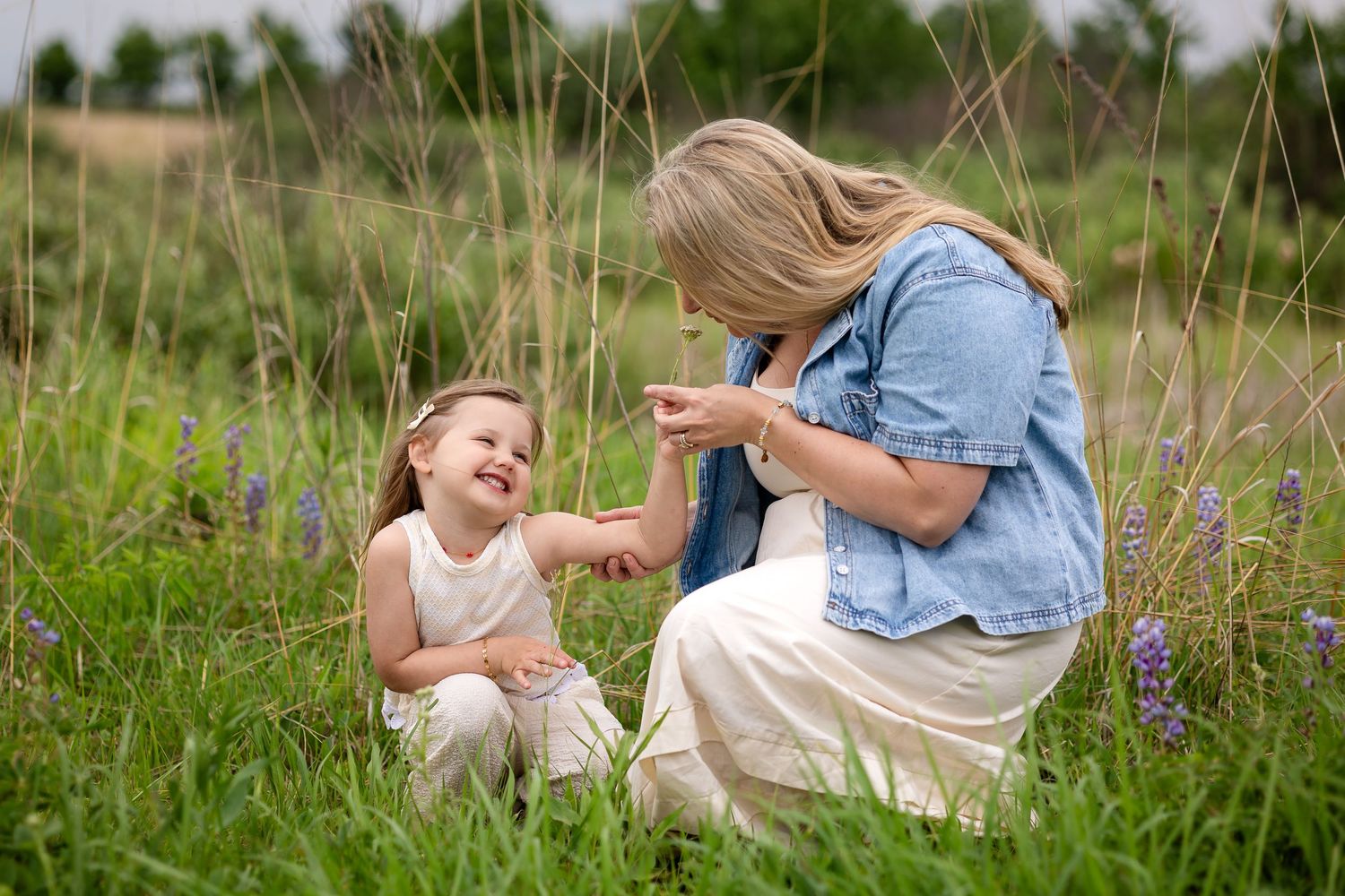 Mother and young daughter laughing together in a wildflower meadow on a sunny day.