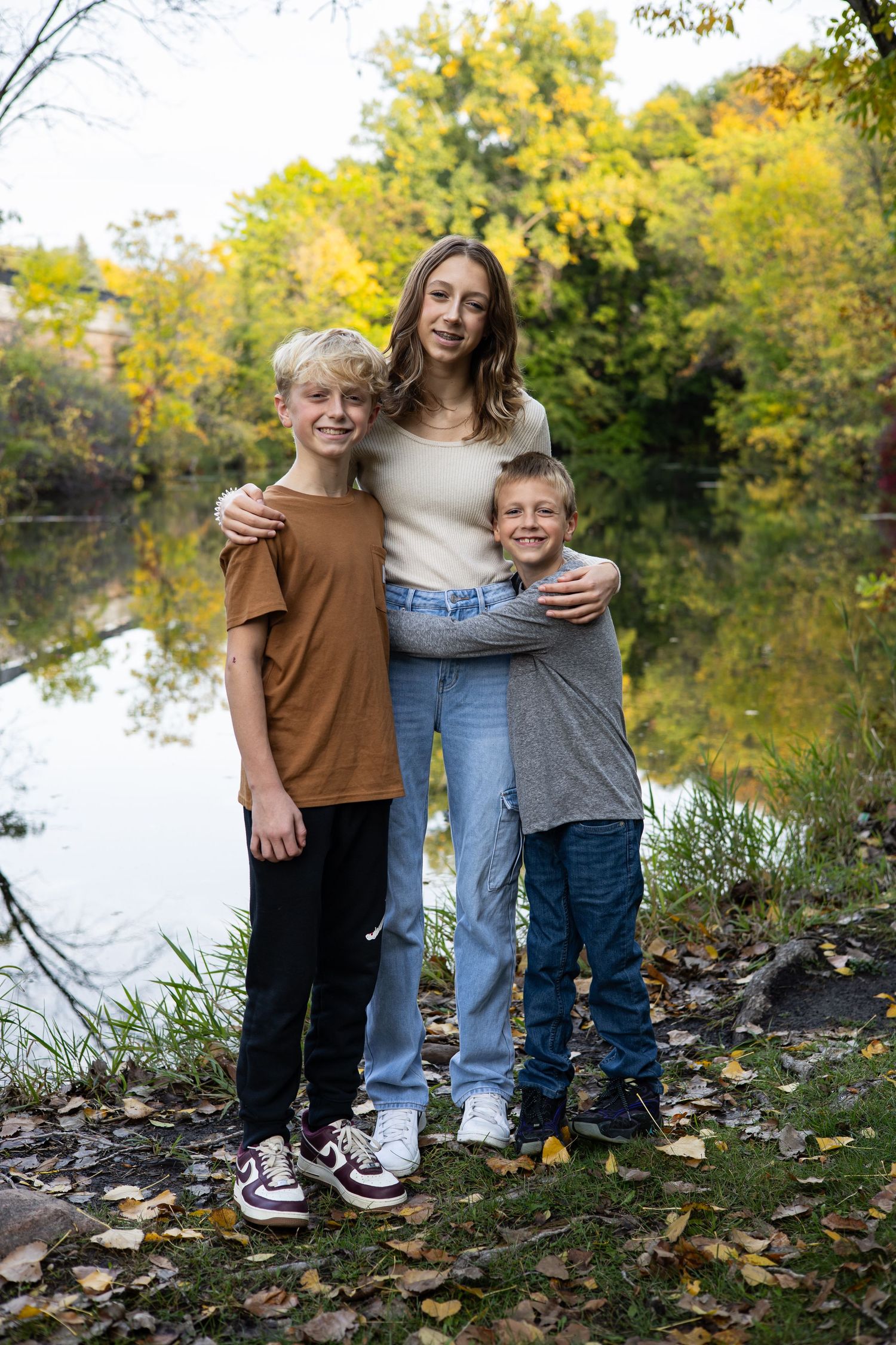 Family posing by autumn lake with fallen leaves on ground.