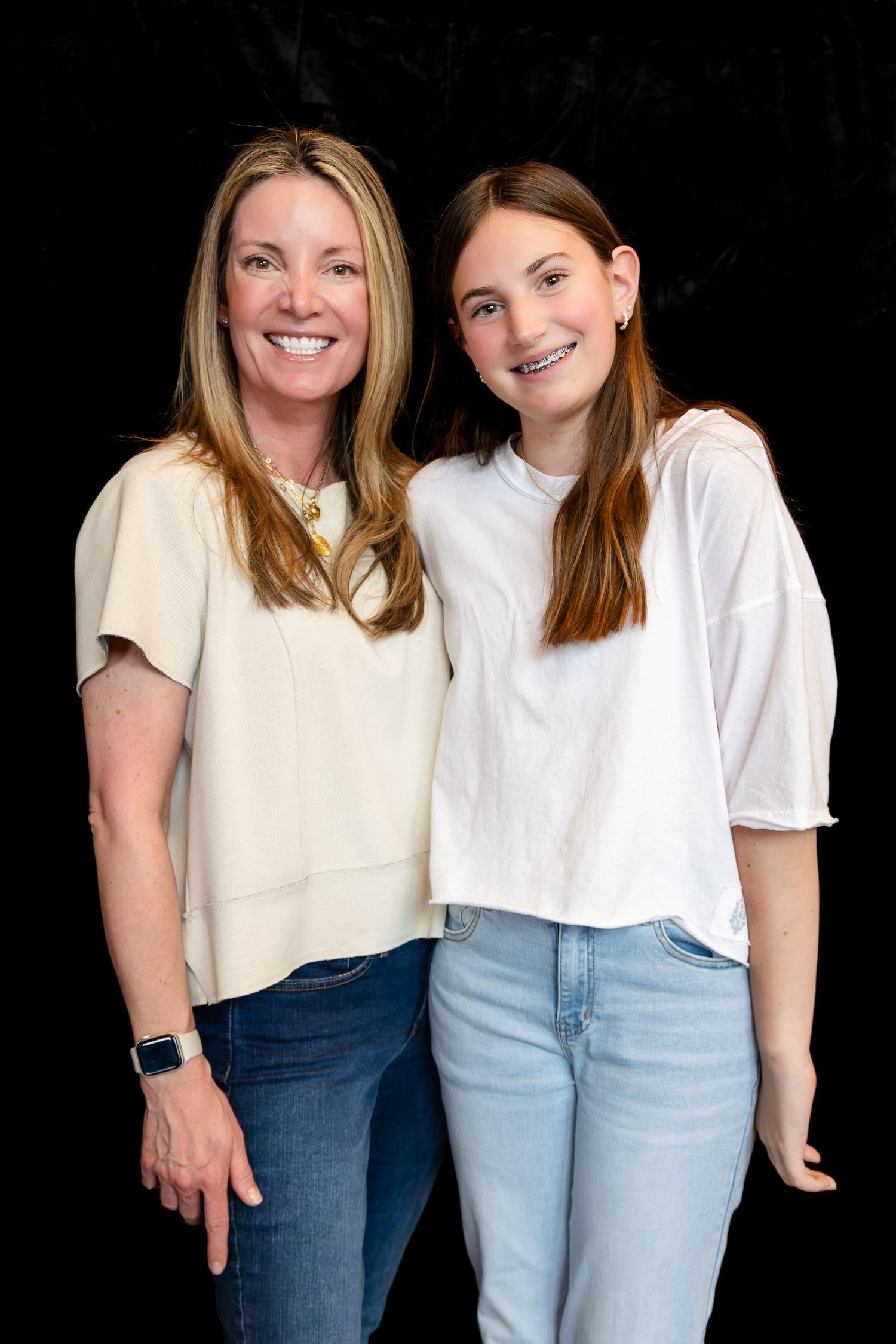 Two people wearing coordinated white tops and denim jeans against black background.