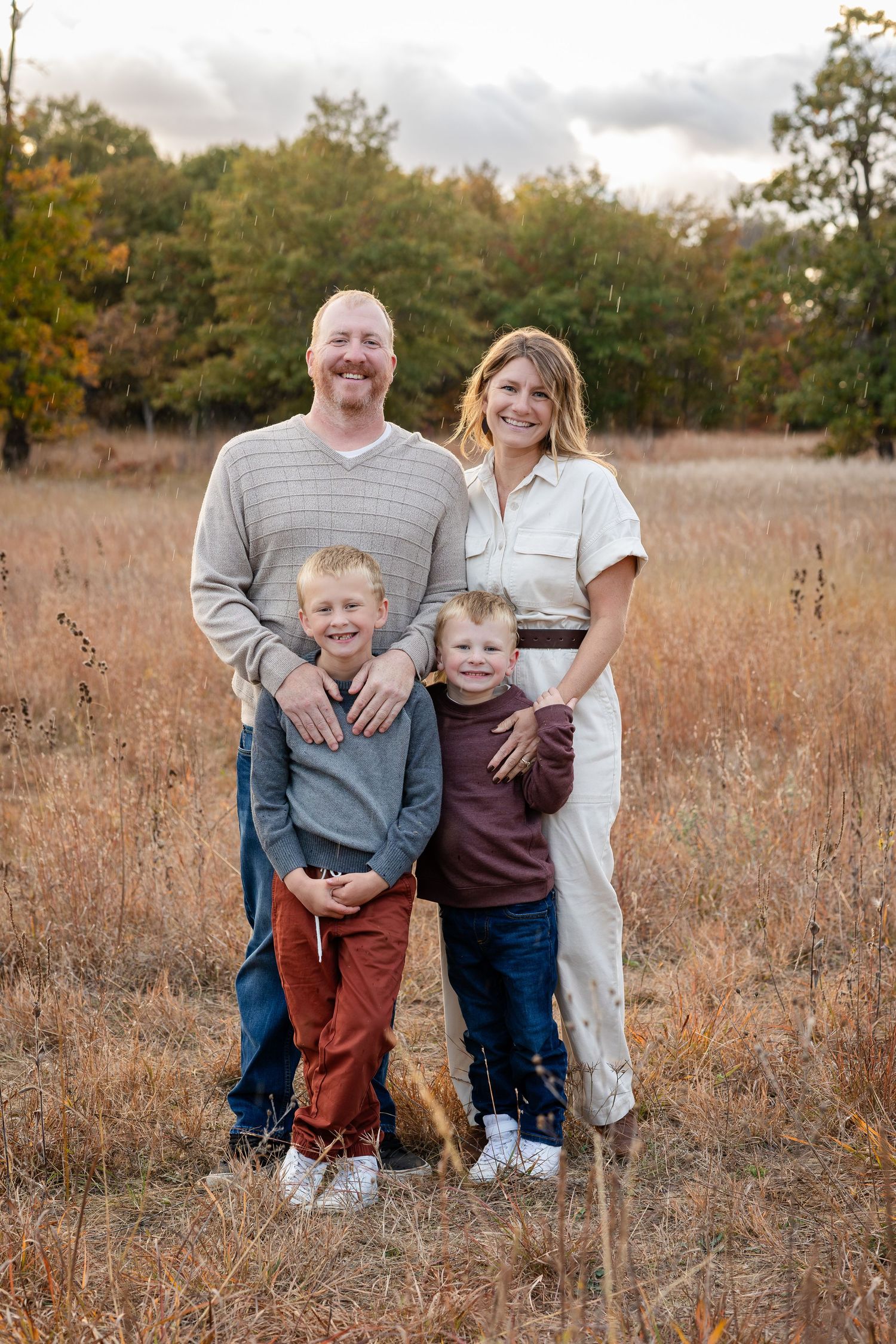 Family portrait in a rustic field with tall grass during golden hour.
