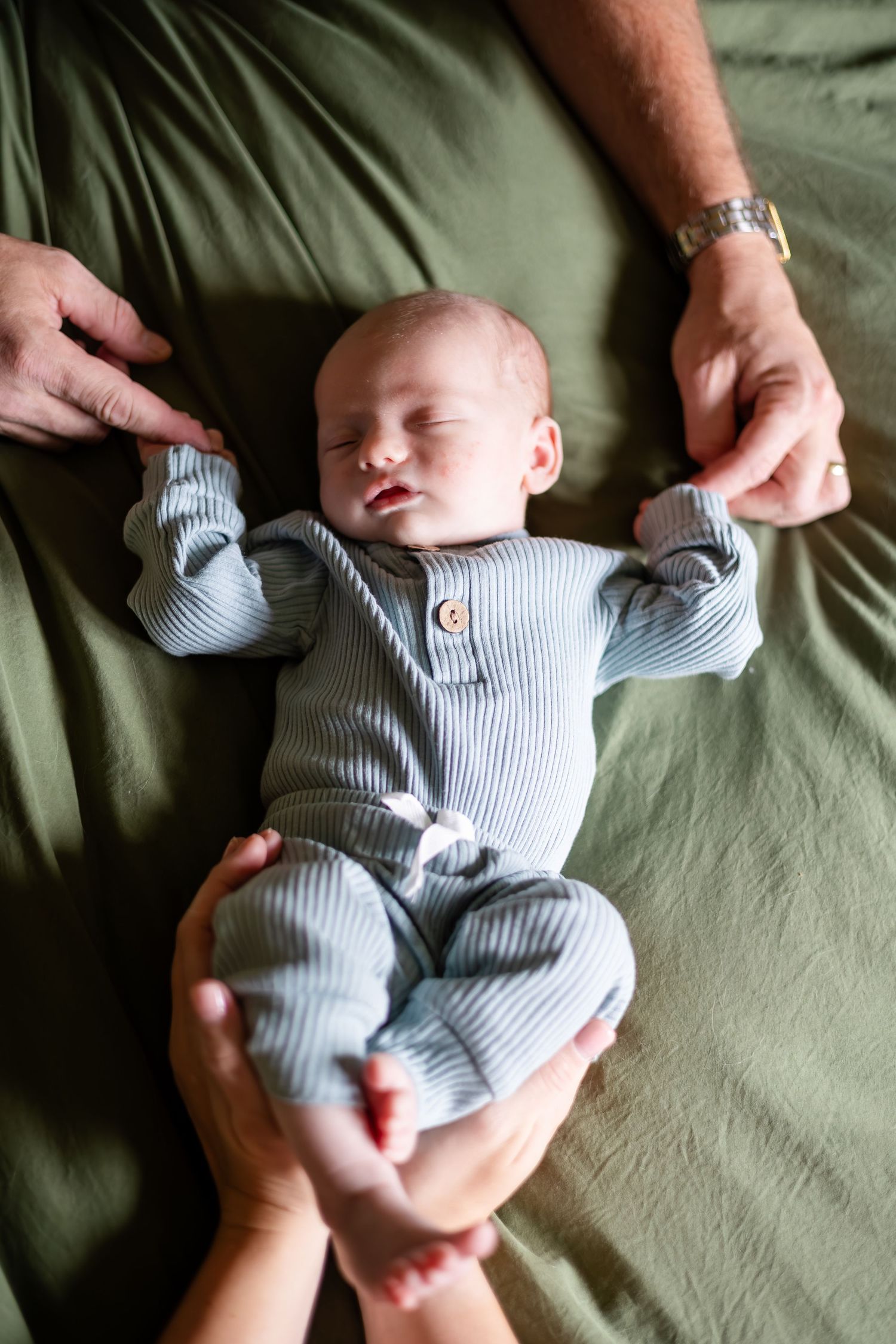 Baby in striped onesie lying on green fabric during lifestyle photoshoot.