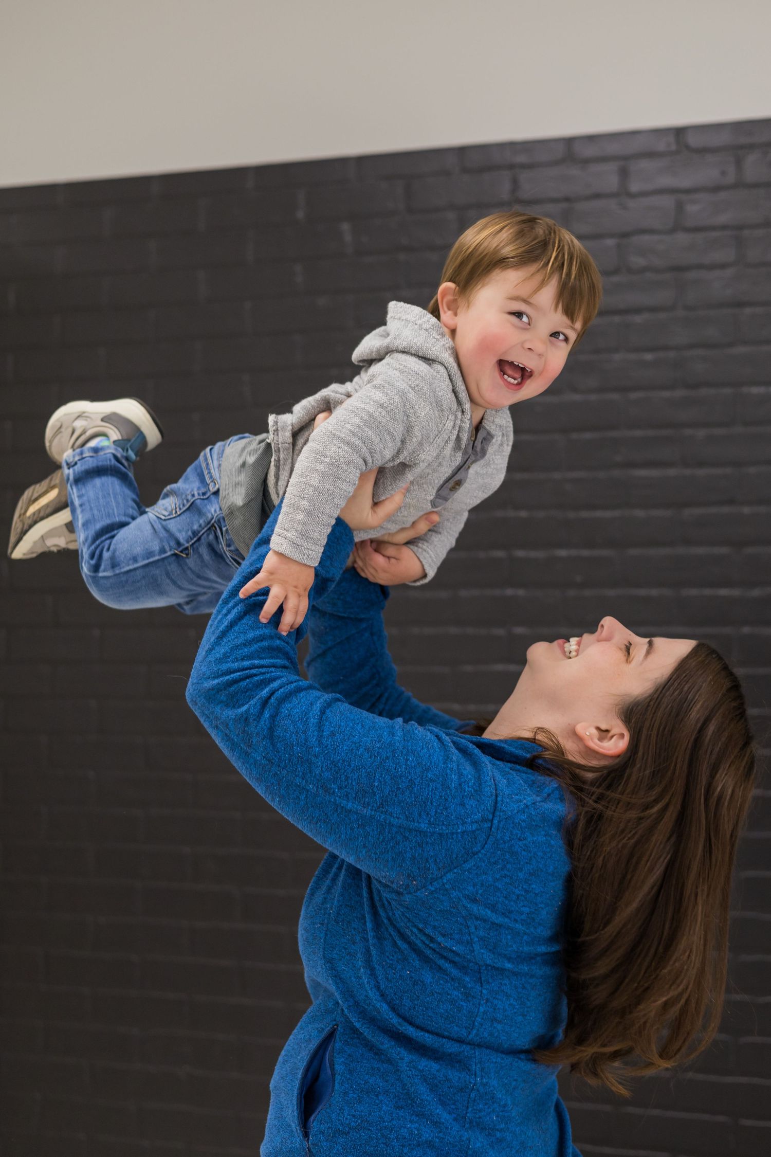 Playful lifting poses between parent and child wearing blue and grey against a dark wall.