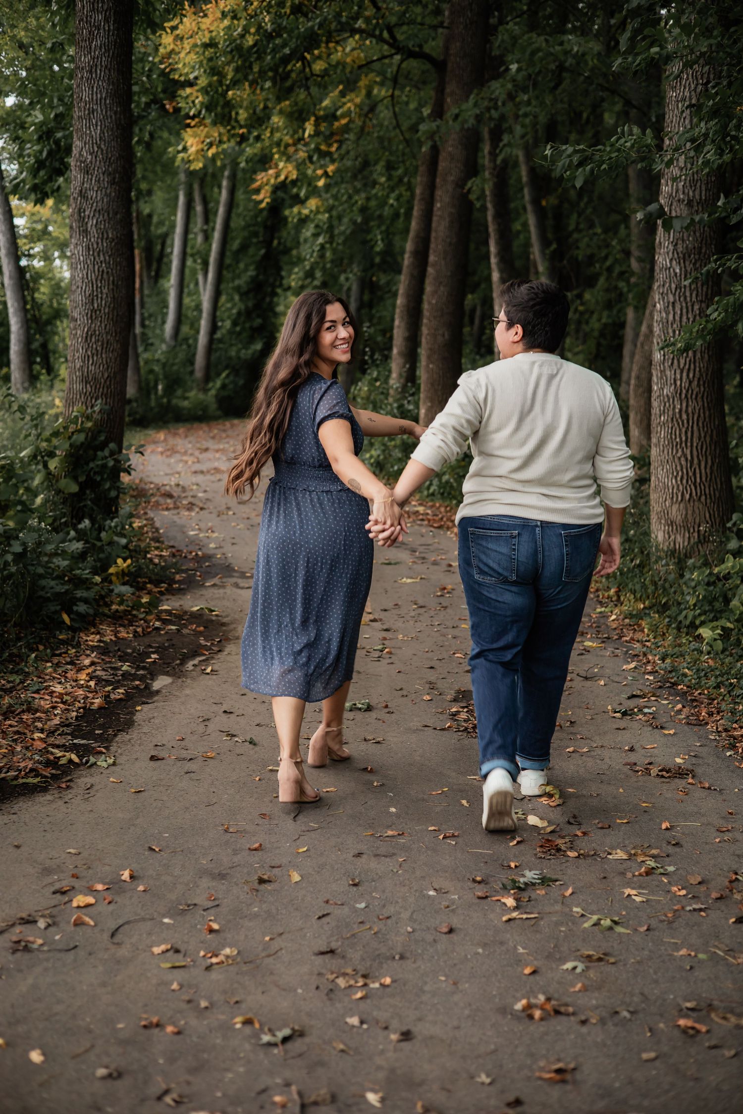 Couple walking hand in hand down a tree-lined autumn path.