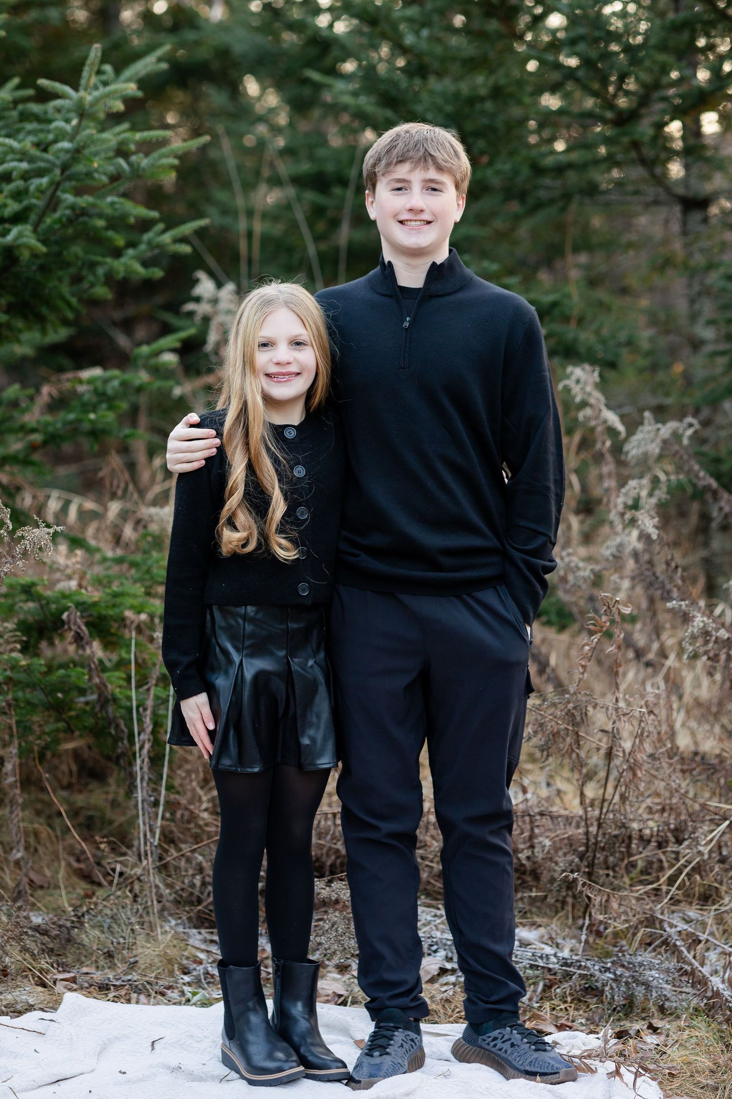 Family members in coordinated black outfits pose together in a natural outdoor setting with fallen leaves.