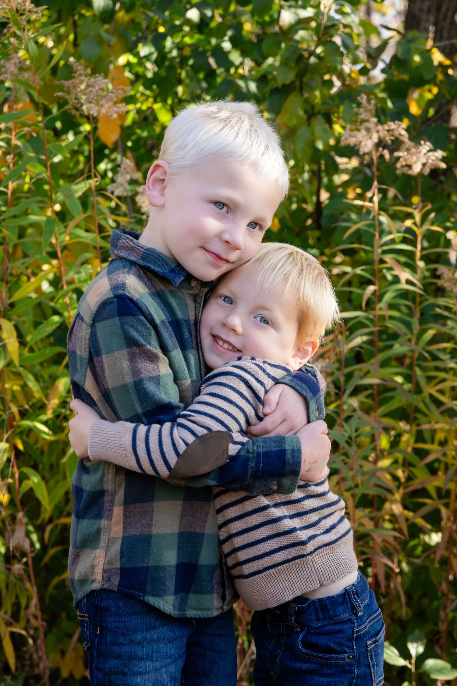 Sweet sibling embrace captured in natural outdoor setting with autumn foliage.