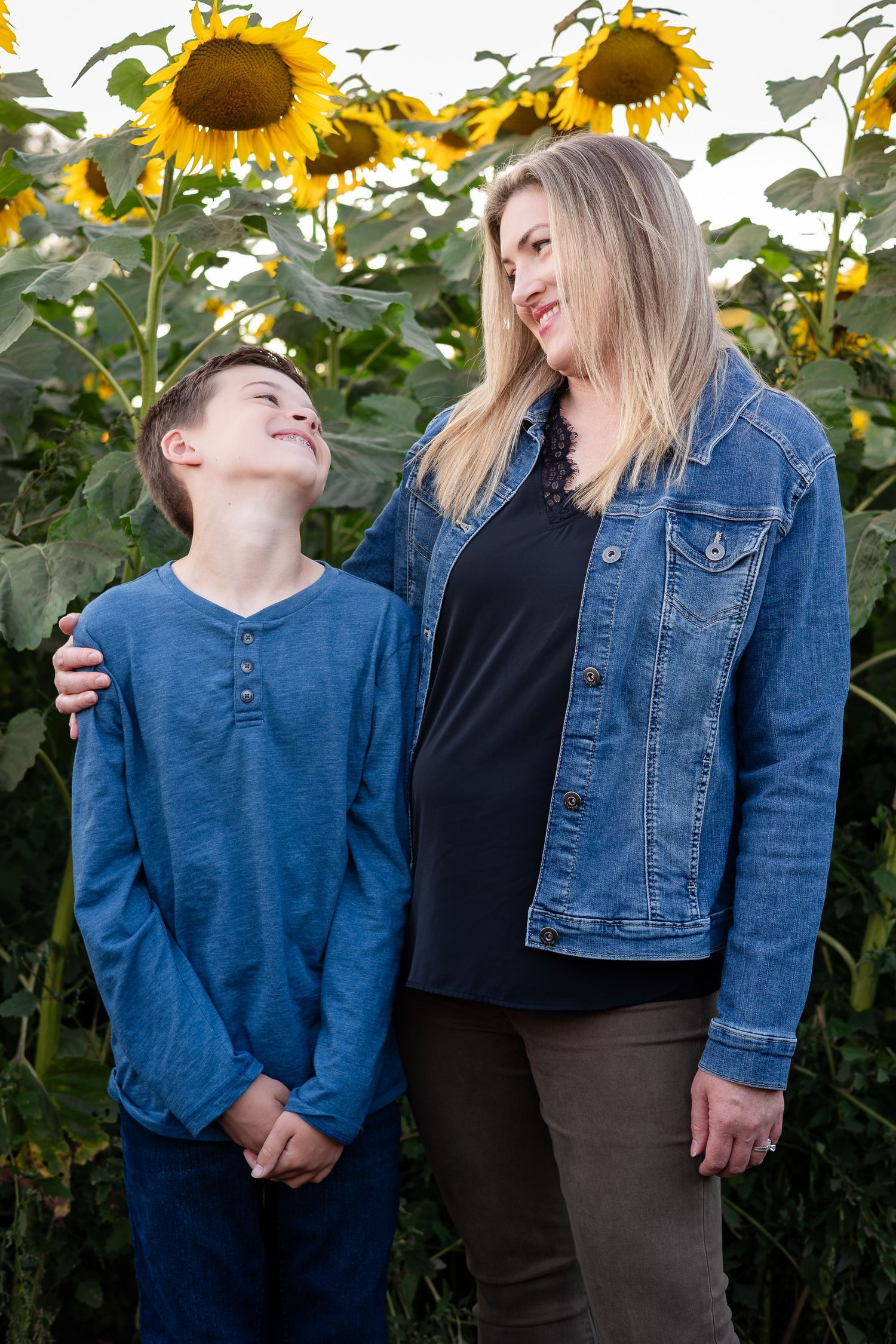 Family members in denim and dark clothing pose casually together among blooming sunflowers.