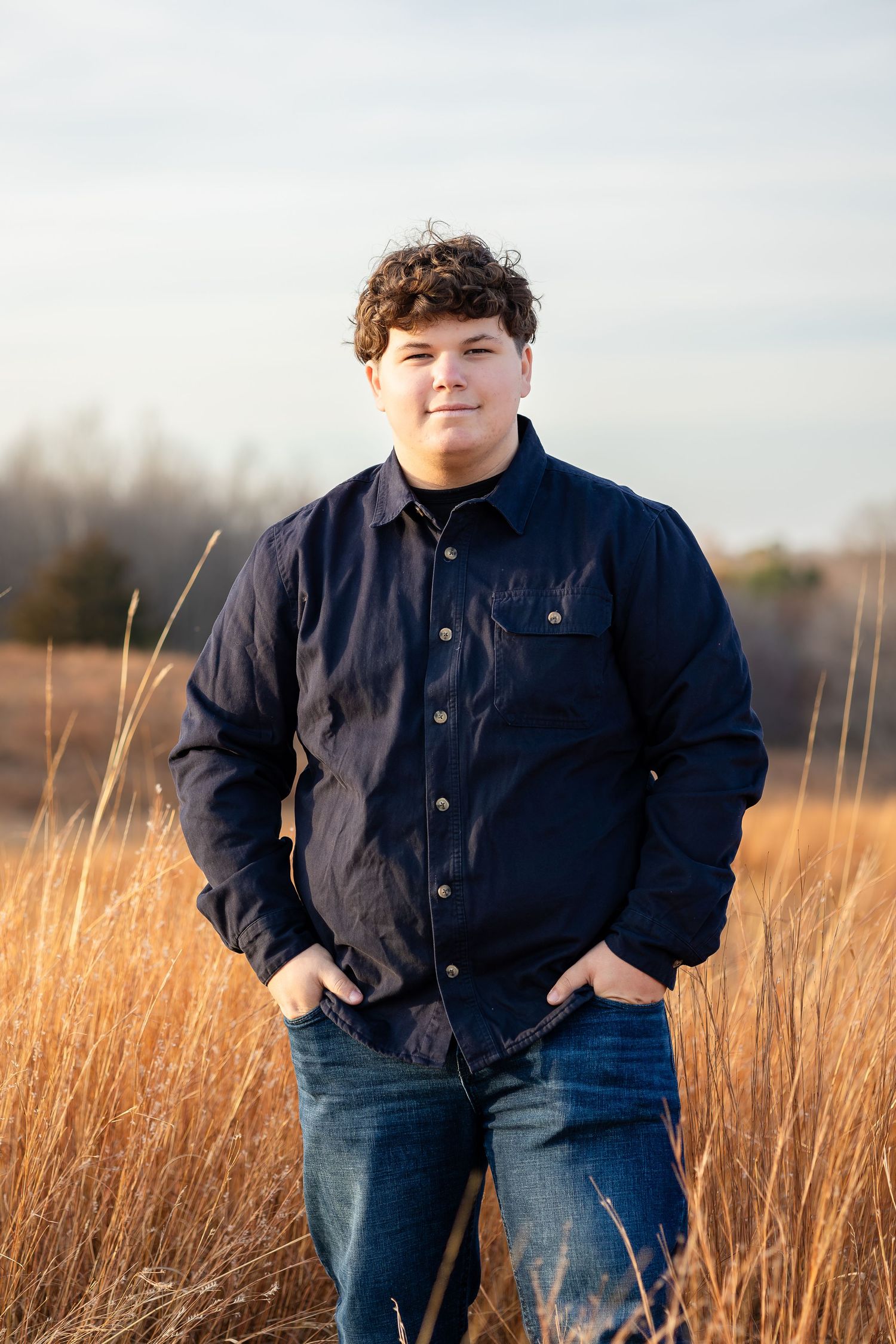 Figure standing in golden prairie grass wearing navy jacket and jeans.