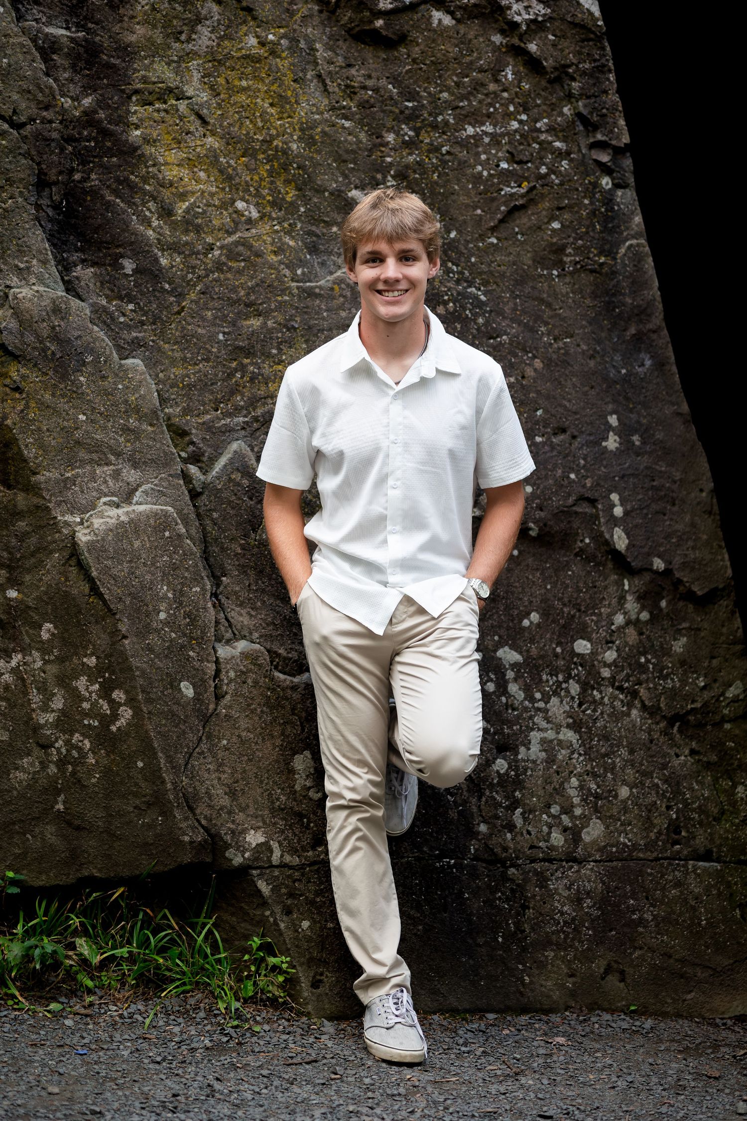 Person in white shirt and khakis leans against textured rock wall outdoors.