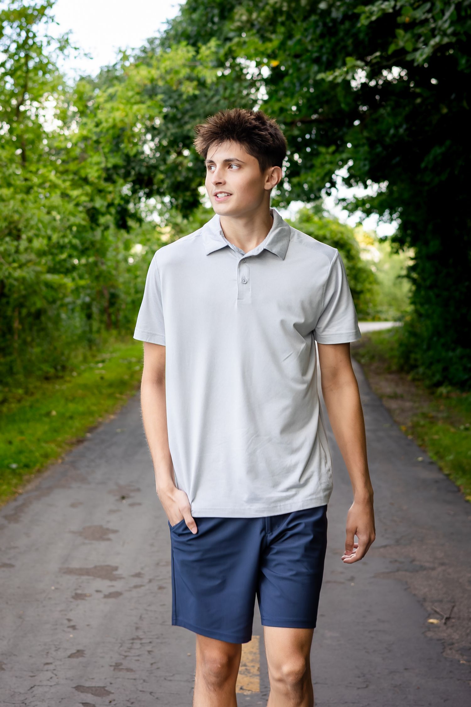 Person walking along a tree-lined path wearing a light polo shirt and navy shorts.