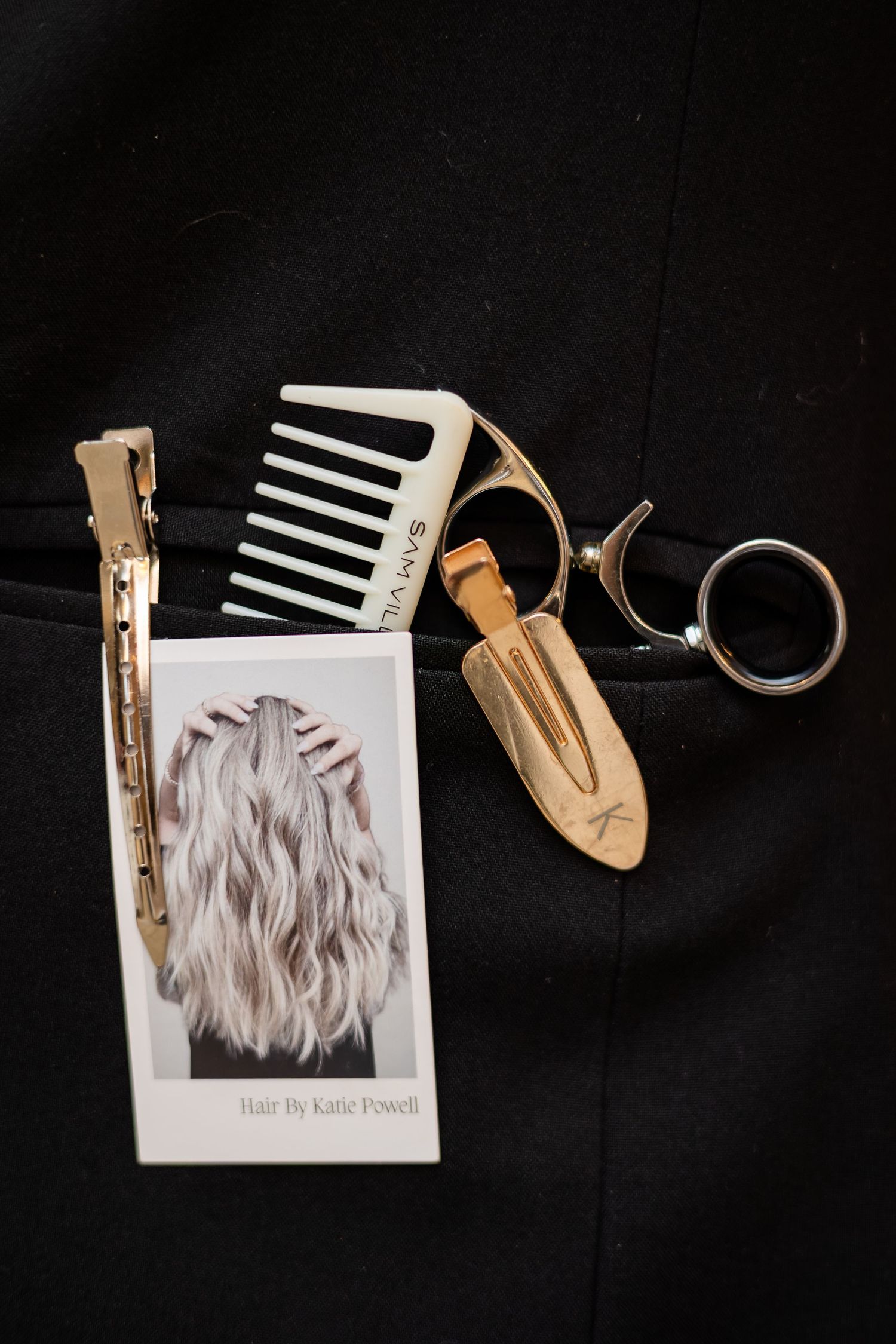 Stylish hair salon marketing flatlay with silver hair photo, gold comb keychain, and scissors on black background.