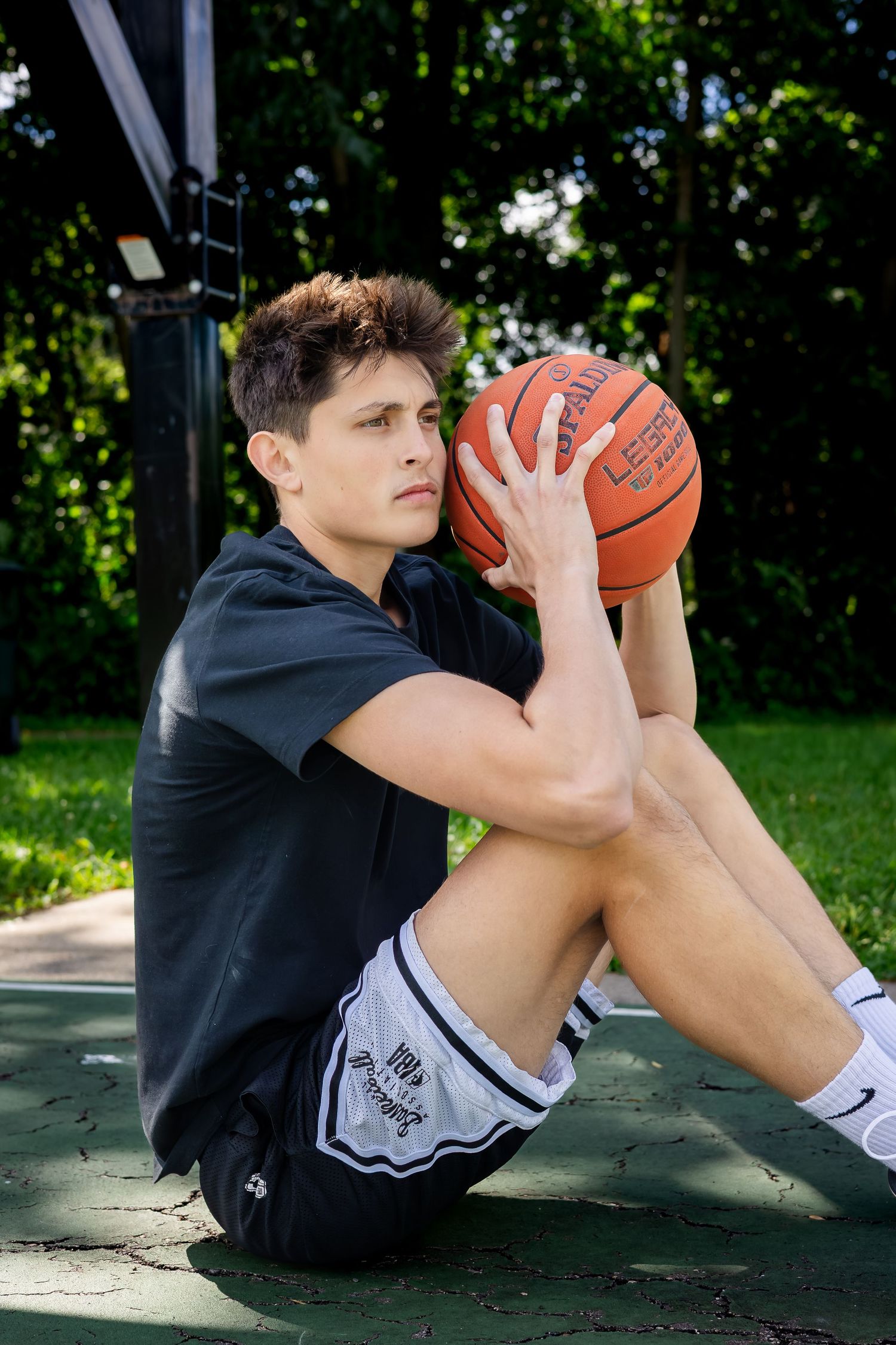 Basketball player in black shirt sitting on court holding ball.