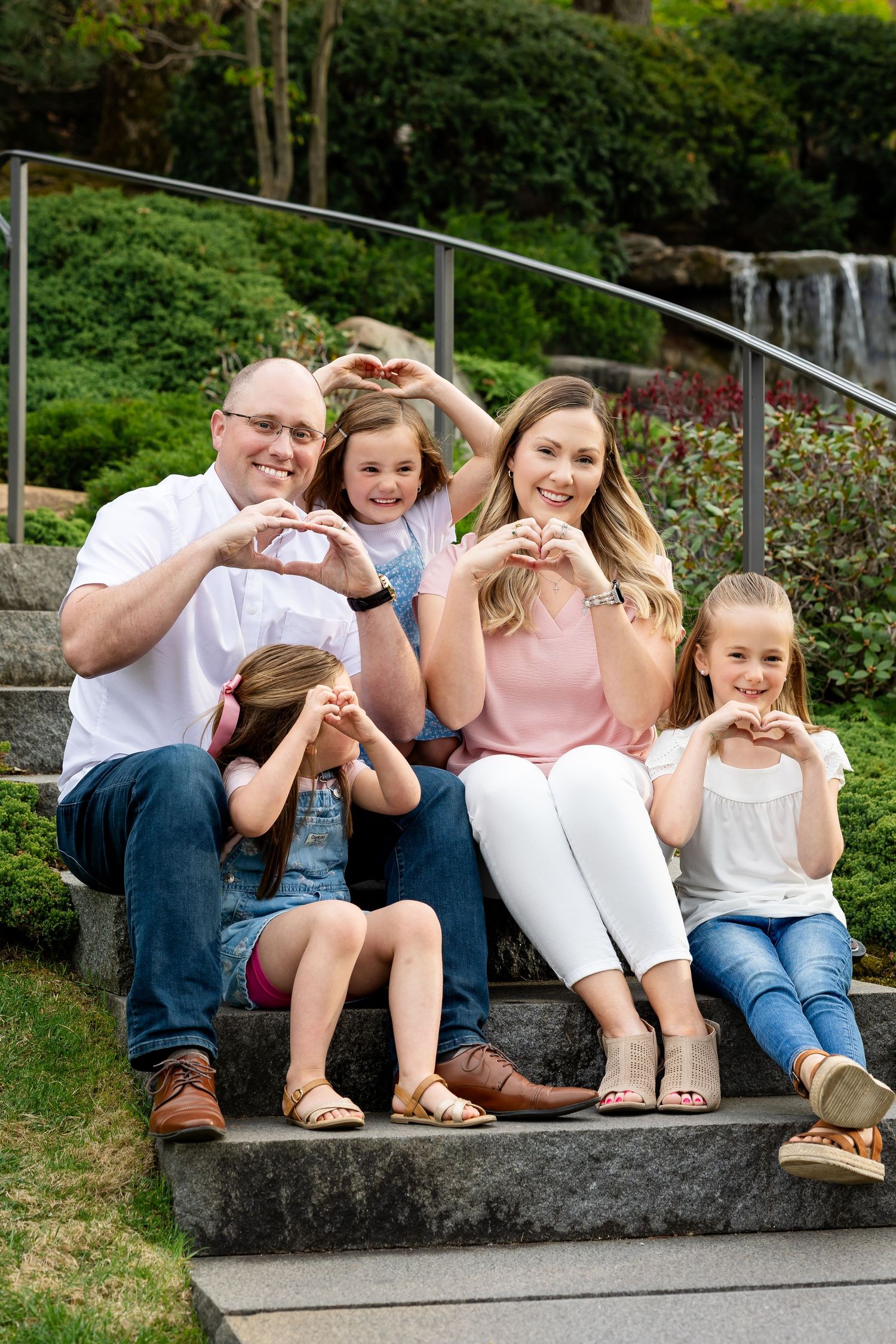 Happy family of five making heart shapes with hands on garden steps near waterfall.