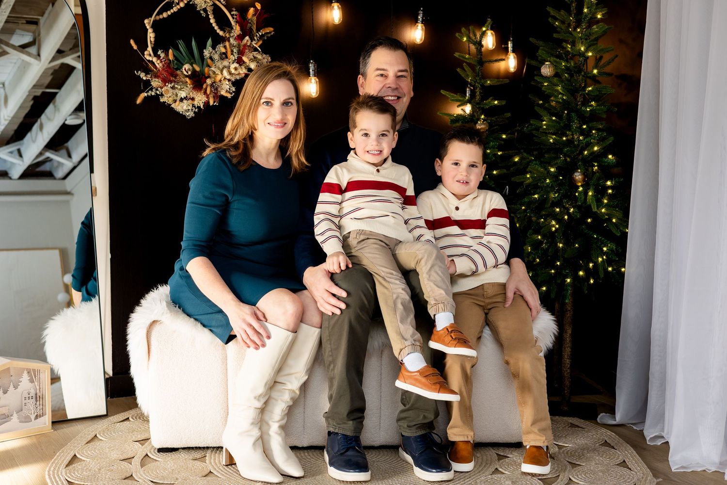 Family of four posing for a Christmas portrait near a decorated tree in a cozy holiday studio setting.