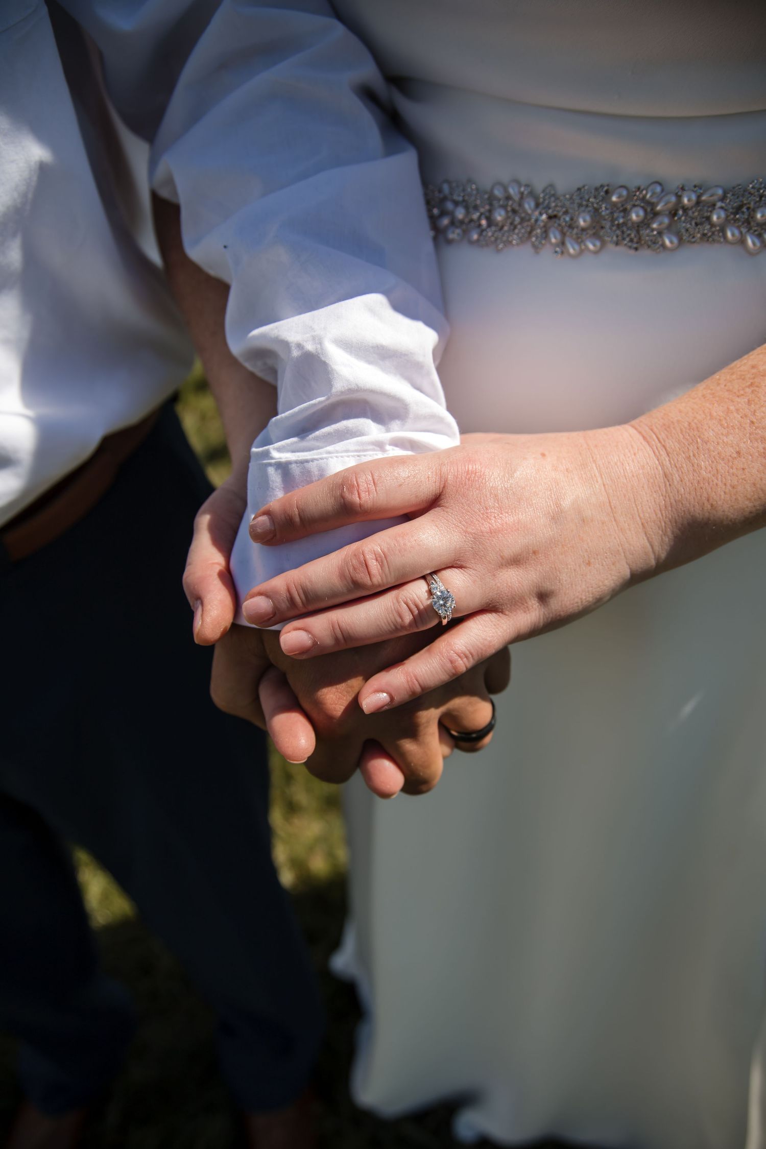 Close-up of wedding rings and joined hands showing intricate bridal details.
