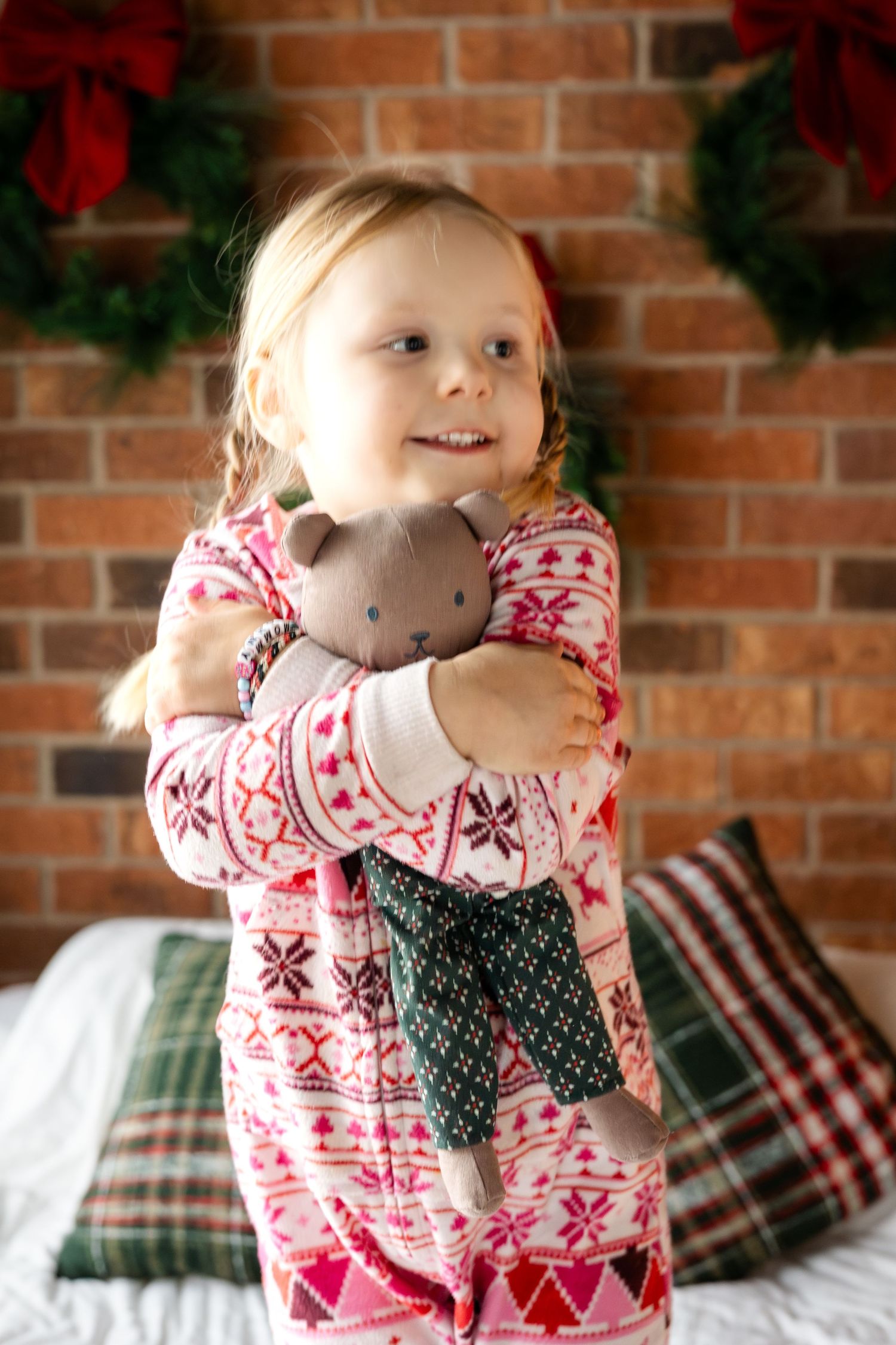 Playful holiday photos in pink Nordic print pajamas against brick wall with Christmas decorations.
