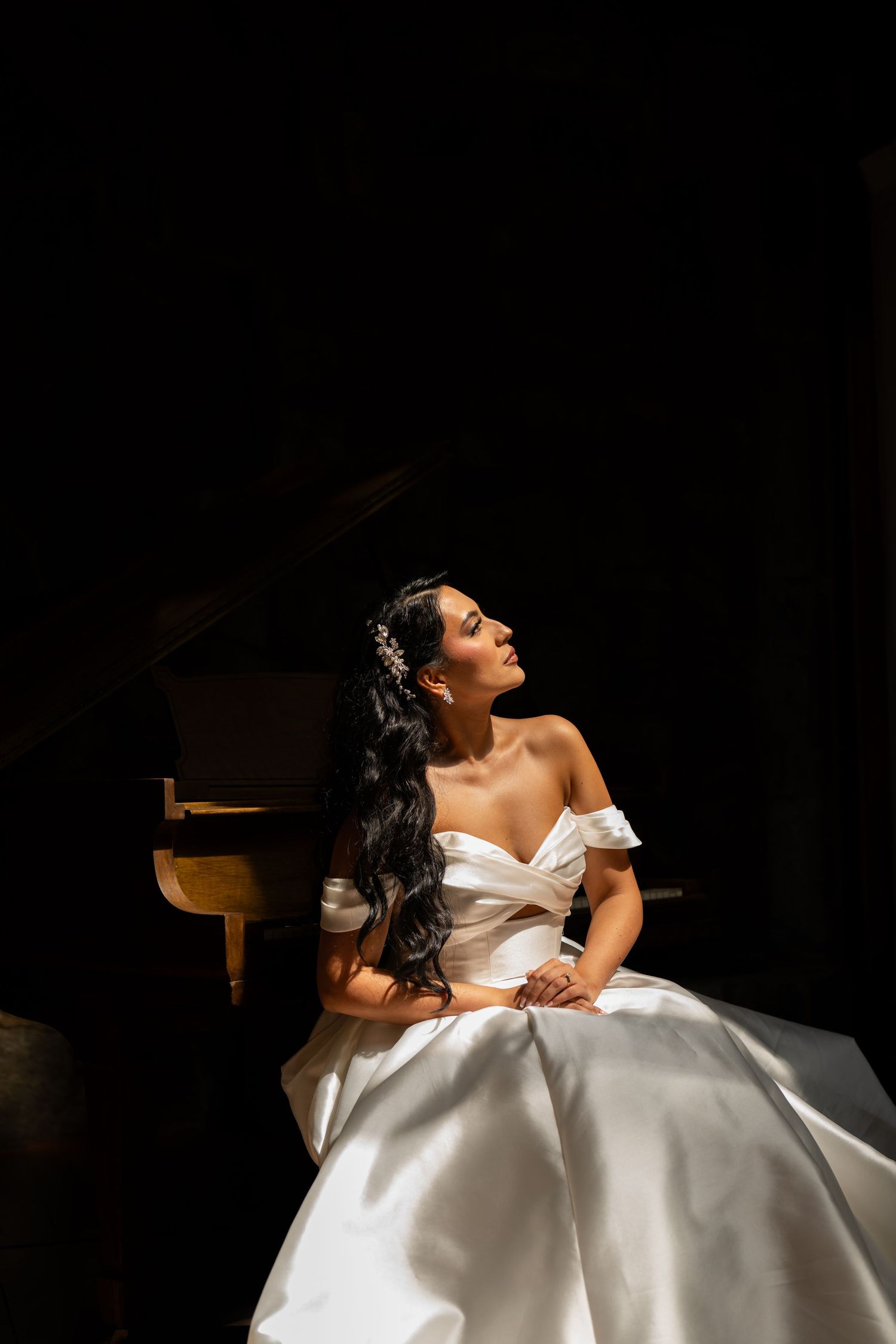 A bride in a white ballgown poses dramatically in dramatic lighting against a dark background.