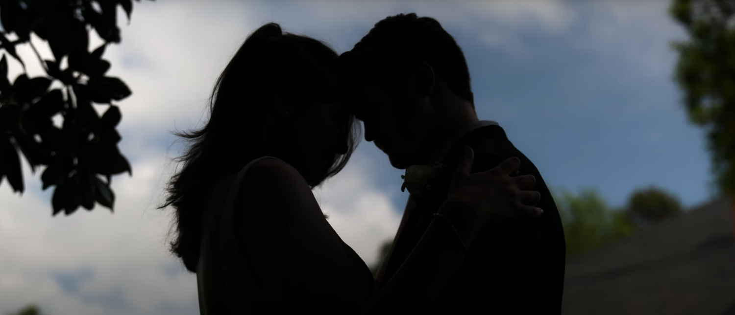 Silhouettes of a couple against a dramatic cloudy sky during sunset.