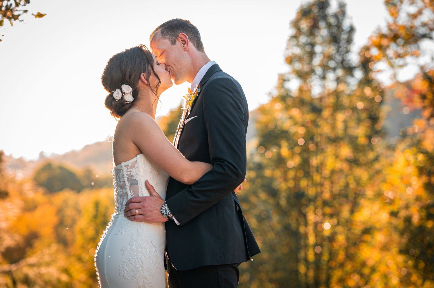 Newlyweds share intimate moment during golden hour with autumn trees in background.