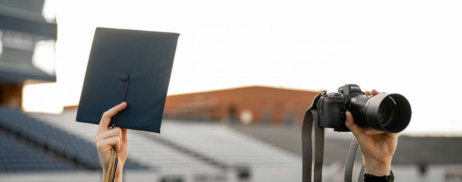 Hands holding up a laptop and camera against stadium seating backdrop.