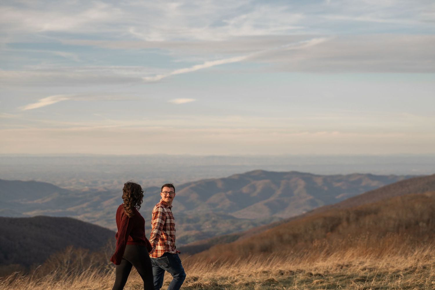 Couple sharing intimate moment on mountain overlook with panoramic vista.