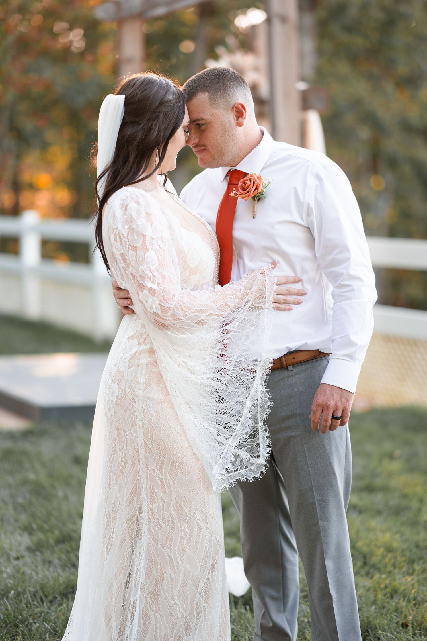 A tender wedding moment captured outdoors with the bride in a lace dress and groom in white shirt.