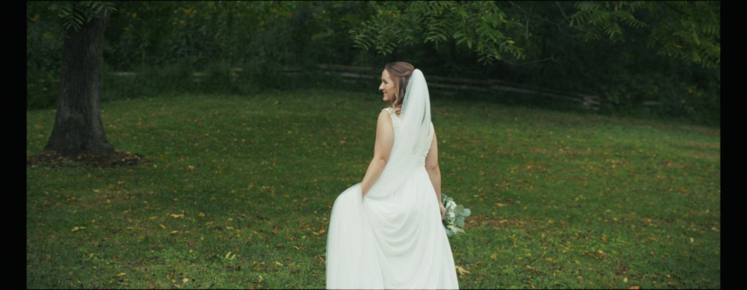Bride in flowing white dress walking through green garden setting.
