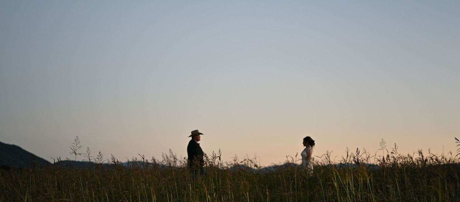 Two silhouettes stand in a field against a sunset sky creating a dramatic scene.